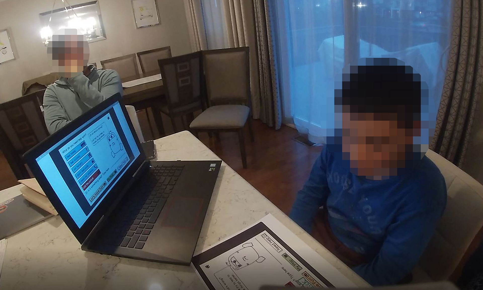 A child seated in front of a laptop, looking at papers on the table.