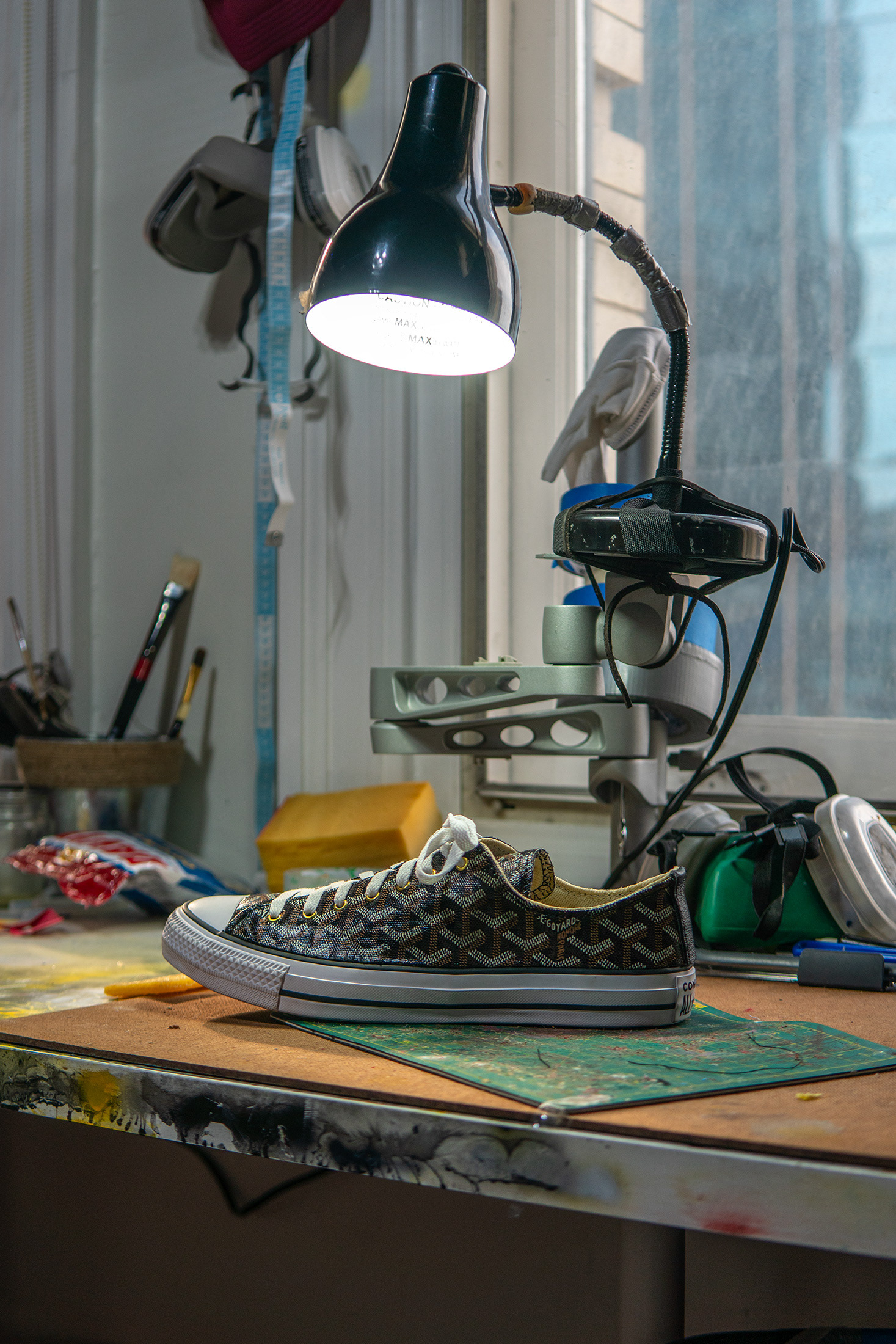 Custom Goyard Converses sitting on a workshop table, organized chaose of art supplies in the background