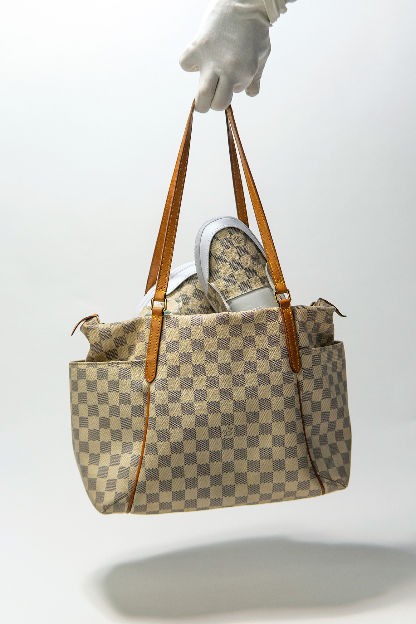 Custom unfinished Louis Vuitton Nike Dunks inside of a Louis Vuitton Damier bag, held infront of a white backdrop