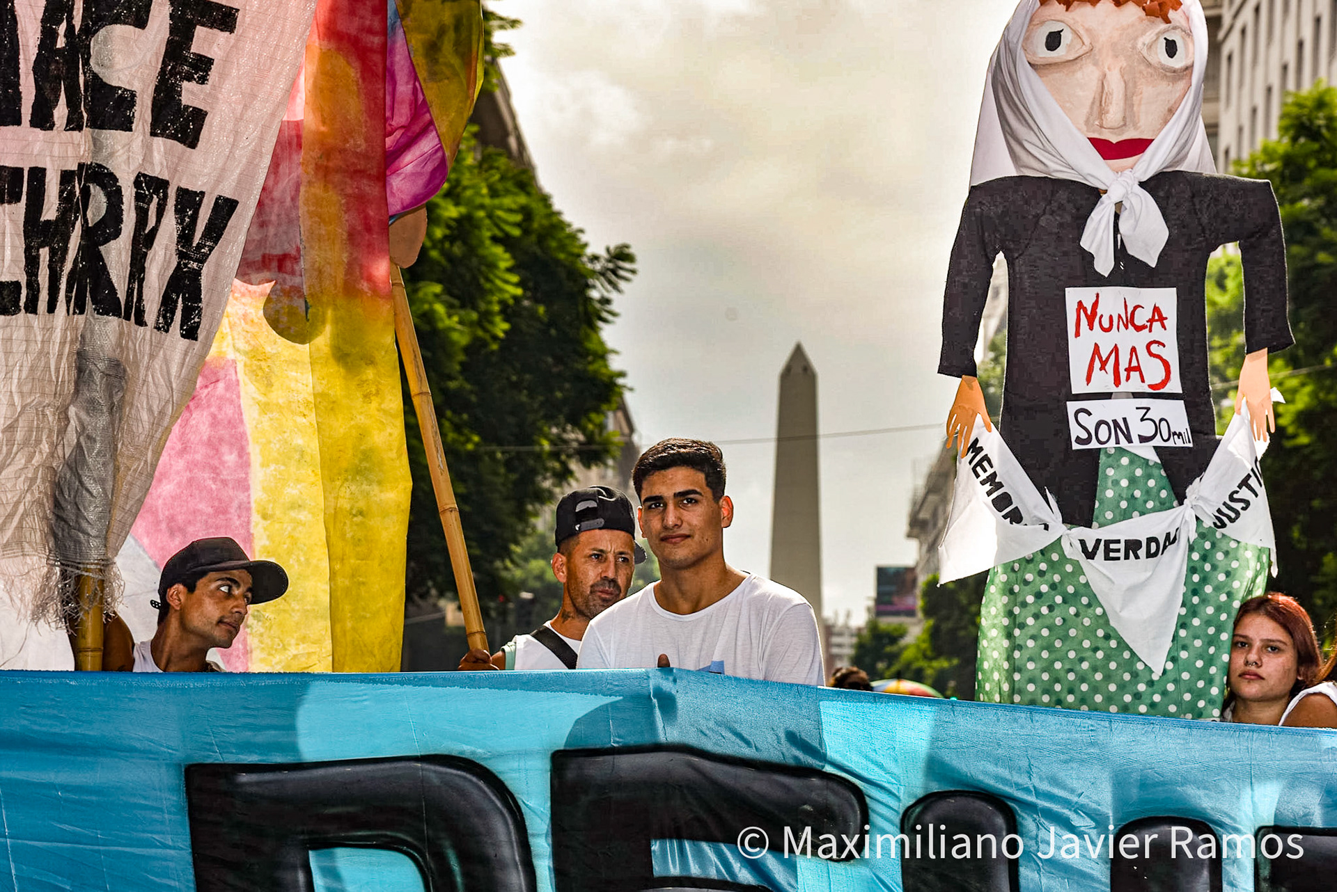 Un grupo de personas marchan por una de las principales avenidas de Buenos Aires con el Obelisco de fondo durante la marcha del Día de la Memoria. / A group of people march through one of the main avenues of Buenos Aires with the Obelisk in the background during the Remembrance Day march. / El Día Nacional de la Memoria por la Verdad y la Justicia es un día feriado inamovible de Argentina que se conmemora cada 24 de marzo. La fecha remite al golpe de Estado del 24 de marzo de 1976 y busca generar memoria y conciencia colectiva para que los golpes de Estado y las violaciones de derechos humanos no se repitan "nunca más" y sus autores sean enjuiciados y castigados. El Proceso de Reorganización Nacional fue una dictadura cívico-militar que causó que decenas de miles de personas fueran asesinadas, desaparecidas, violadas, torturadas, secuestradas siendo bebés, o debieran nacer en cautiverio, padecer la sustracción de su identidad y sufrir el exilio. Las organizaciones de derechos humanos, los sindicatos, el movimiento estudiantil, los movimientos sociales y muchos partidos políticos hacen referencia a los 30 000 desaparecidos,1 que fueron víctimas de la última dictadura y cuya presencia en la sociedad actual se invoca en cada conmemoración al grito “30.000 detenidos-desaparecidos ¡Presentes! ¡Ahora y siempre!” The National Day of Memory for Truth and Justice is an immovable holiday in Argentina that is commemorated every March 24. The date refers to the coup d'état of March 24, 1976 and seeks to generate memory and collective awareness so that coups d'état and human rights violations are not repeated "never again" and their perpetrators are prosecuted and punished. The National Reorganization Process was a civil-military dictatorship that caused tens of thousands of people to be killed, disappeared, raped, tortured, kidnapped as babies, or had to be born in captivity, suffer theft of their identity and suffer exile. Human rights organizations, trade unions, the student movement, social movements and many political parties refer to the 30,000 disappeared,1 who were victims of the last dictatorship and whose presence in today's society is invoked in every shouted commemoration “30,000 detained-disappeared Present! Now and always!"