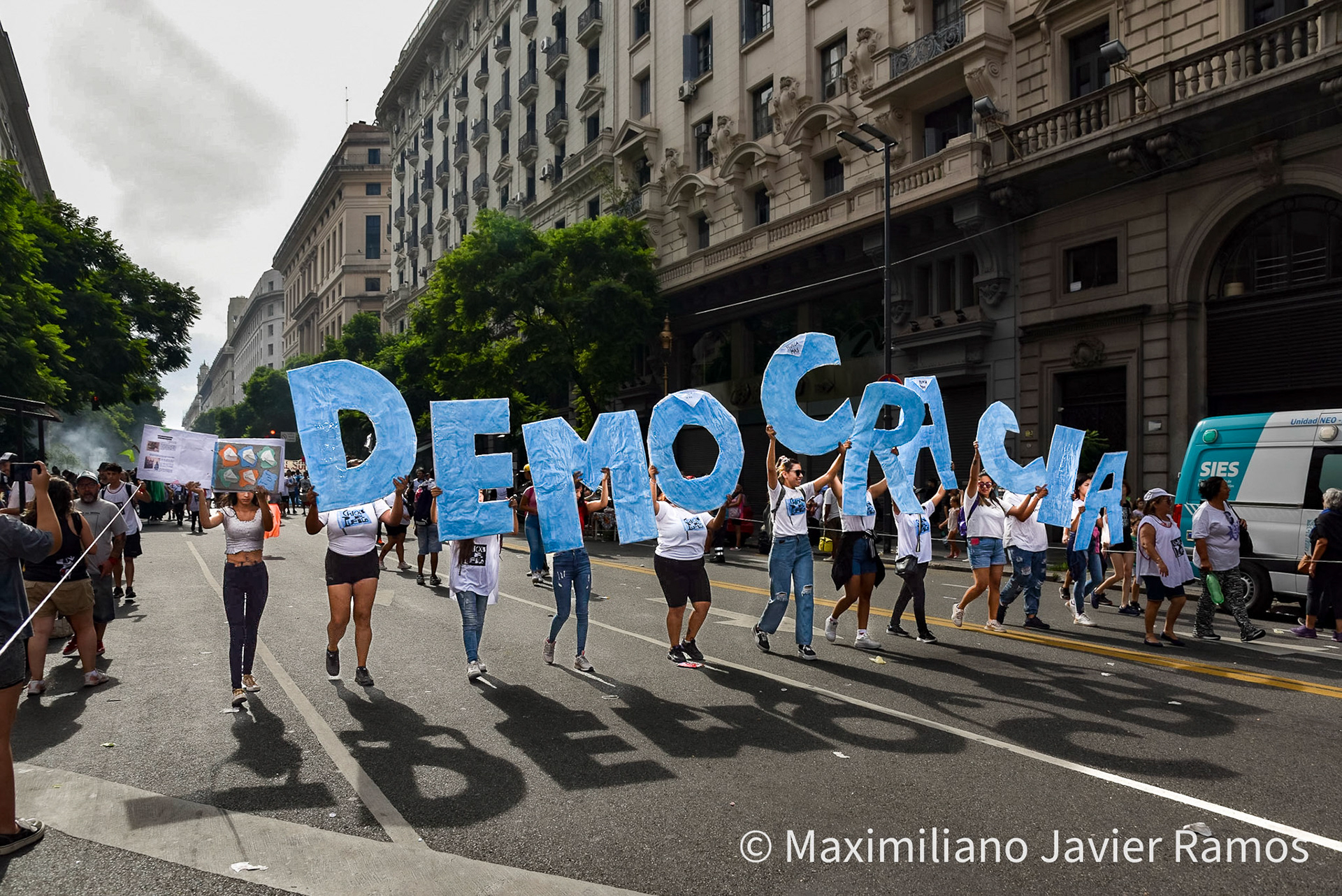 Un grupo de personas marchan por una de las principales avenidas de Buenos Aires con letras gigantes que forman la palabra “Democracia” durante la marcha del Día de la Memoria. / A group of people march down one of the main avenues of Buenos Aires with giant letters spelling the word "Democracy" during the Remembrance Day march. / El Día Nacional de la Memoria por la Verdad y la Justicia es un día feriado inamovible de Argentina que se conmemora cada 24 de marzo. La fecha remite al golpe de Estado del 24 de marzo de 1976 y busca generar memoria y conciencia colectiva para que los golpes de Estado y las violaciones de derechos humanos no se repitan "nunca más" y sus autores sean enjuiciados y castigados. El Proceso de Reorganización Nacional fue una dictadura cívico-militar que causó que decenas de miles de personas fueran asesinadas, desaparecidas, violadas, torturadas, secuestradas siendo bebés, o debieran nacer en cautiverio, padecer la sustracción de su identidad y sufrir el exilio. Las organizaciones de derechos humanos, los sindicatos, el movimiento estudiantil, los movimientos sociales y muchos partidos políticos hacen referencia a los 30 000 desaparecidos,1 que fueron víctimas de la última dictadura y cuya presencia en la sociedad actual se invoca en cada conmemoración al grito “30.000 detenidos-desaparecidos ¡Presentes! ¡Ahora y siempre!” / The National Day of Memory for Truth and Justice is an immovable holiday in Argentina that is commemorated every March 24. The date refers to the coup d'état of March 24, 1976 and seeks to generate memory and collective awareness so that coups d'état and human rights violations are not repeated "never again" and their perpetrators are prosecuted and punished. The National Reorganization Process was a civil-military dictatorship that caused tens of thousands of people to be killed, disappeared, raped, tortured, kidnapped as babies, or had to be born in captivity, suffer theft of their identity and suffer exile. Human rights organizations, trade unions, the student movement, social movements and many political parties refer to the 30,000 disappeared,1 who were victims of the last dictatorship and whose presence in today's society is invoked in every shouted commemoration “30,000 detained-disappeared Present! Now and always!"