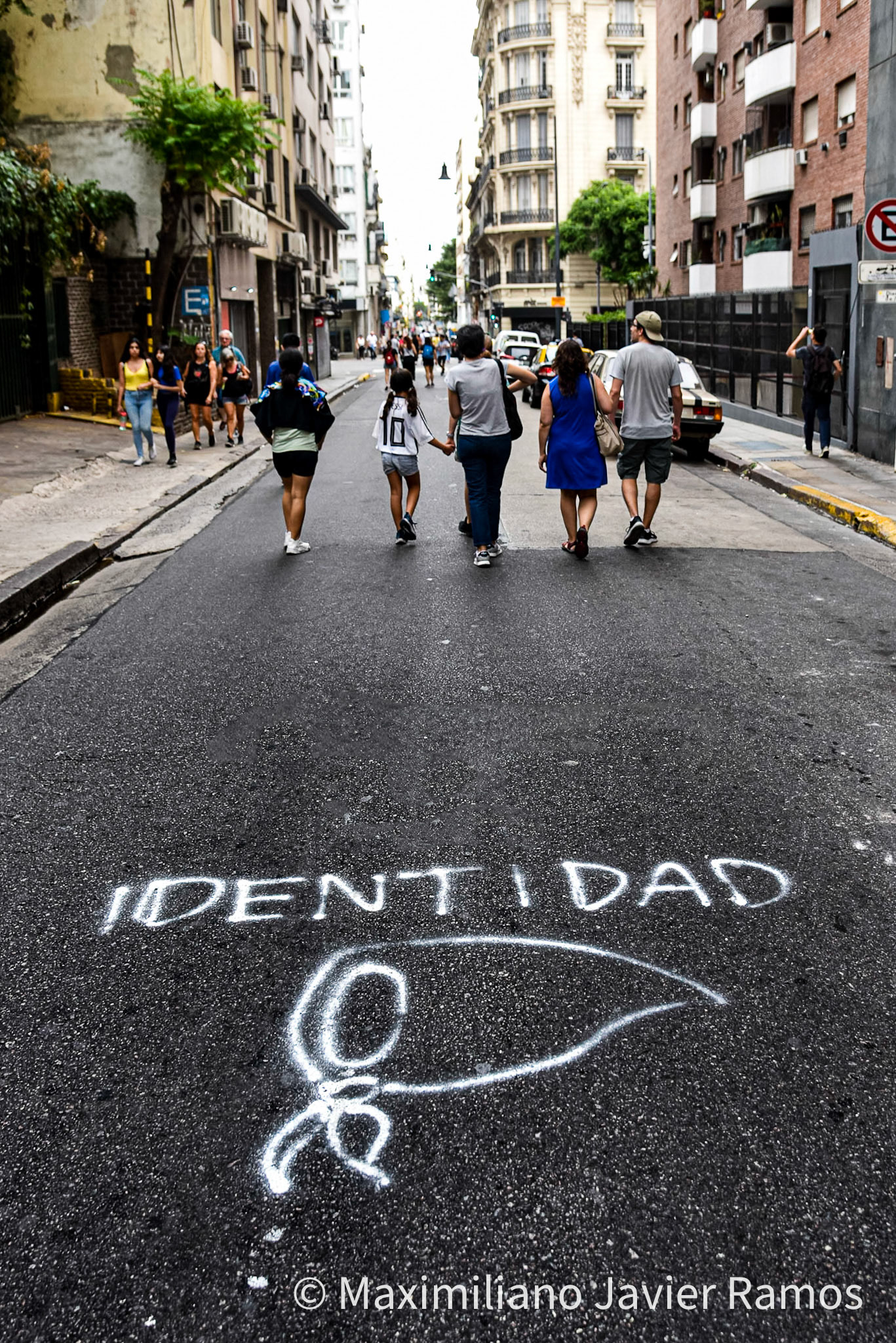 Familias vuelven a sus casas por una calle de Buenos Aires, intervenida con un grafitti con la palabra "Identidad" y una pañuelo blanco, símbolo de las Madres y Abuelas de Plaza de Mayo; luego de la marcha por el Día de la Memoria. / Families return to their homes through a street in Buenos Aires, intervened with a graffiti with the word "Identity" and a white handkerchief, symbol of the Mothers and Grandmothers of Plaza de Mayo; after the march for Remembrance Day. / El Día Nacional de la Memoria por la Verdad y la Justicia es un día feriado inamovible de Argentina que se conmemora cada 24 de marzo. La fecha remite al golpe de Estado del 24 de marzo de 1976 y busca generar memoria y conciencia colectiva para que los golpes de Estado y las violaciones de derechos humanos no se repitan "nunca más" y sus autores sean enjuiciados y castigados. El Proceso de Reorganización Nacional fue una dictadura cívico-militar que causó que decenas de miles de personas fueran asesinadas, desaparecidas, violadas, torturadas, secuestradas siendo bebés, o debieran nacer en cautiverio, padecer la sustracción de su identidad y sufrir el exilio. Las organizaciones de derechos humanos, los sindicatos, el movimiento estudiantil, los movimientos sociales y muchos partidos políticos hacen referencia a los 30 000 desaparecidos,1 que fueron víctimas de la última dictadura y cuya presencia en la sociedad actual se invoca en cada conmemoración al grito “30.000 detenidos-desaparecidos ¡Presentes! ¡Ahora y siempre!” / The National Day of Memory for Truth and Justice is an immovable holiday in Argentina that is commemorated every March 24. The date refers to the coup d'état of March 24, 1976 and seeks to generate memory and collective awareness so that coups d'état and human rights violations are not repeated "never again" and their perpetrators are prosecuted and punished. The National Reorganization Process was a civil-military dictatorship that caused tens of thousands of people to be killed, disappeared, raped, tortured, kidnapped as babies, or had to be born in captivity, suffer theft of their identity and suffer exile. Human rights organizations, trade unions, the student movement, social movements and many political parties refer to the 30,000 disappeared,1 who were victims of the last dictatorship and whose presence in today's society is invoked in every shouted commemoration “30,000 detained-disappeared Present! Now and always!"