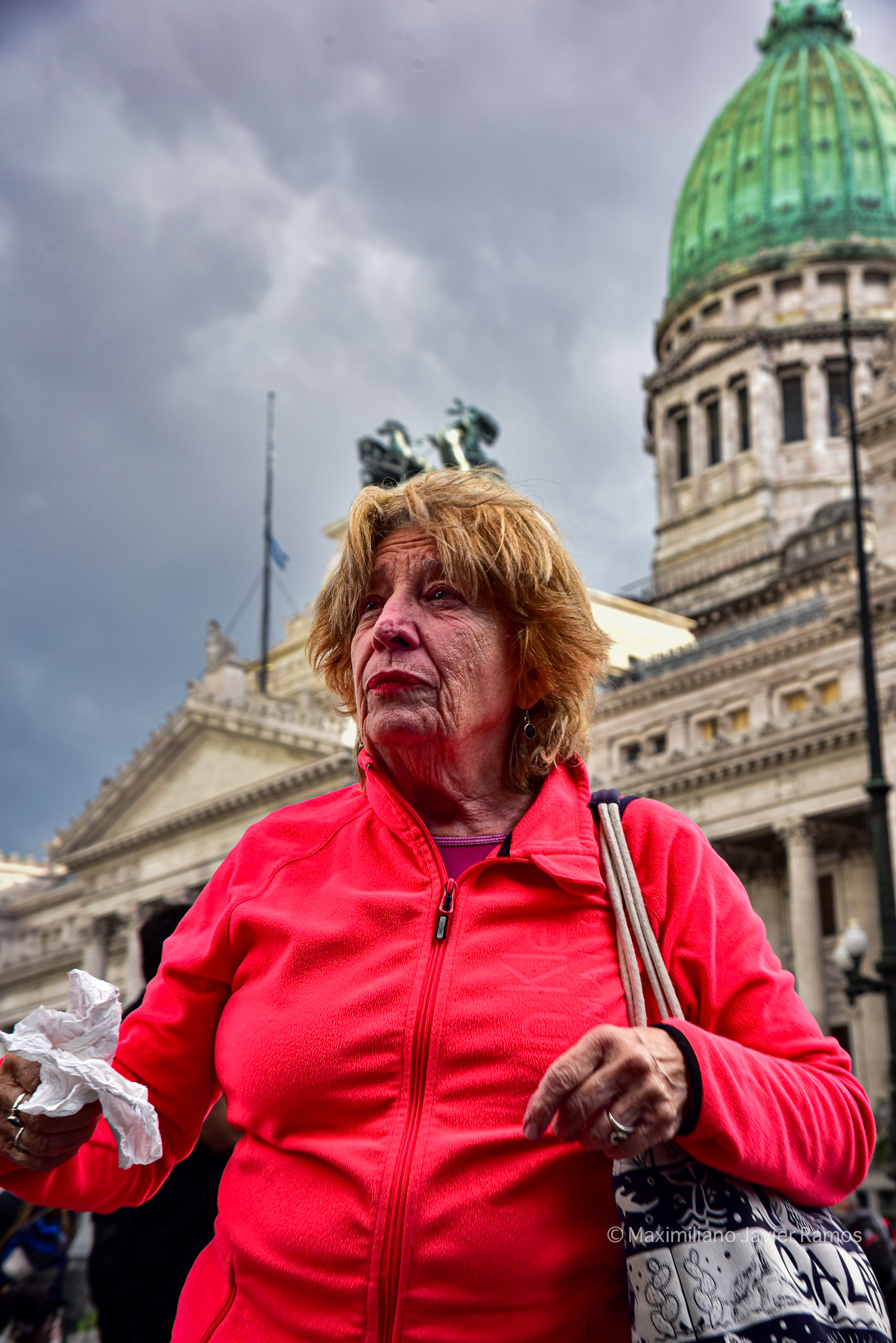 Una jubilada con el rostro enrojecido por el gas antidisturbios utilizado por la policía durante la manifestación. El Congreso Nacional está al fondo. // A retired woman with her face reddened by the riot gas used by police during the demonstration. The National Congress is in the background.