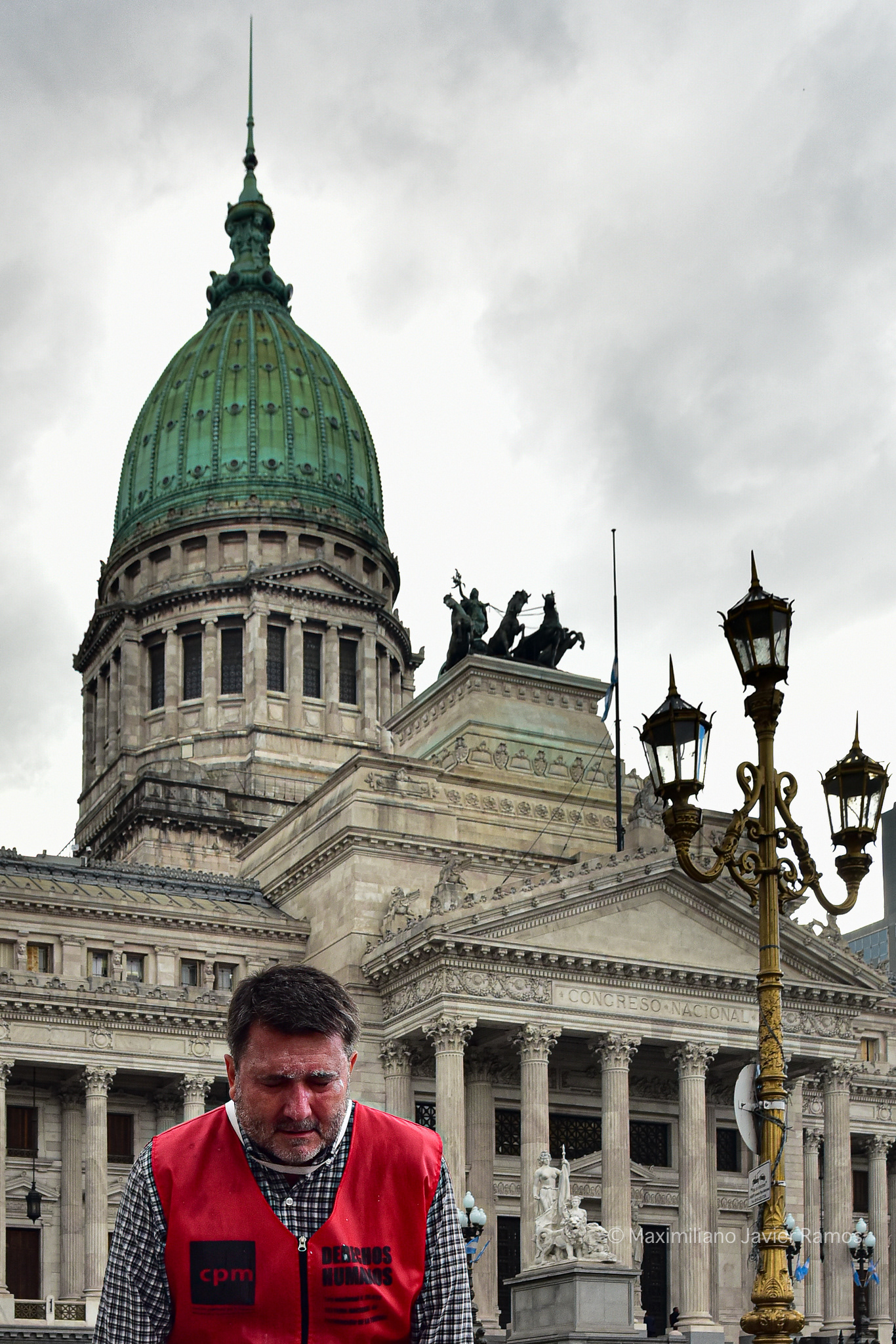 Un hombre, miembro de la Comisión Provincial por la Memoria (CPM), afectado por gases lacrimógenos. Al fondo, el Congreso Nacional Argentino. // A man, a member of the Provincial Commission for Memory (CPM), affected by tear gas. The Argentine National Congress is in the background.