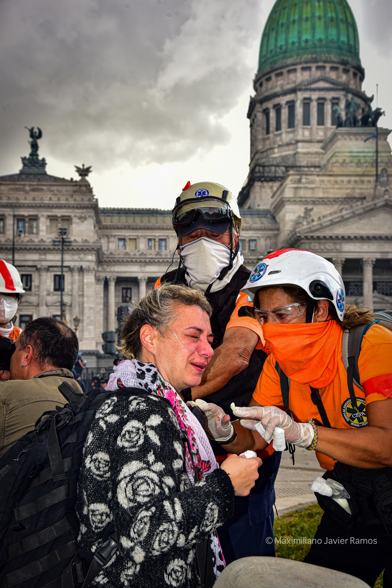 Una mujer afectada por gases lacrimógenos recibe asistencia de miembros de equipos de emergencia autoconvocados. Al fondo, el Congreso Nacional Argentino. // A woman affected by tear gas is assisted by members of self-convened emergency teams. The Argentine National Congress is in the background.