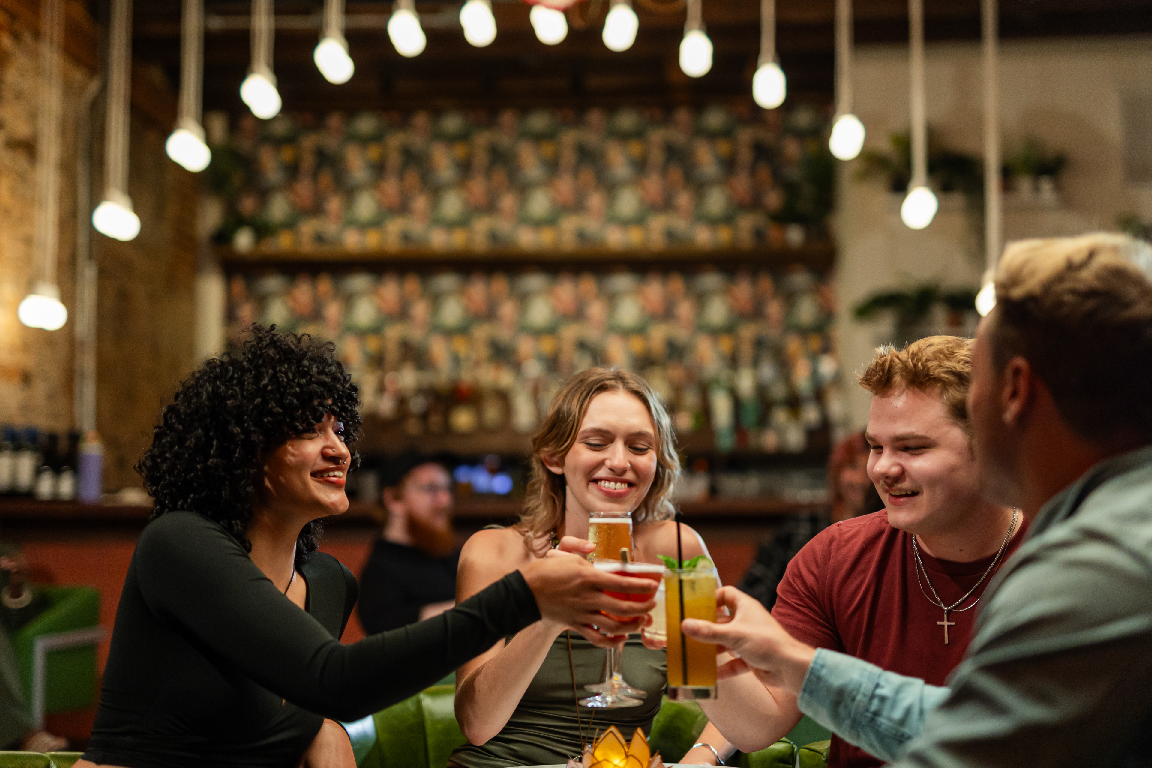 A group of friends smiling and clinking cocktails at Sneak and Dawdle-- a Speak Easy in Opelika Alabama 