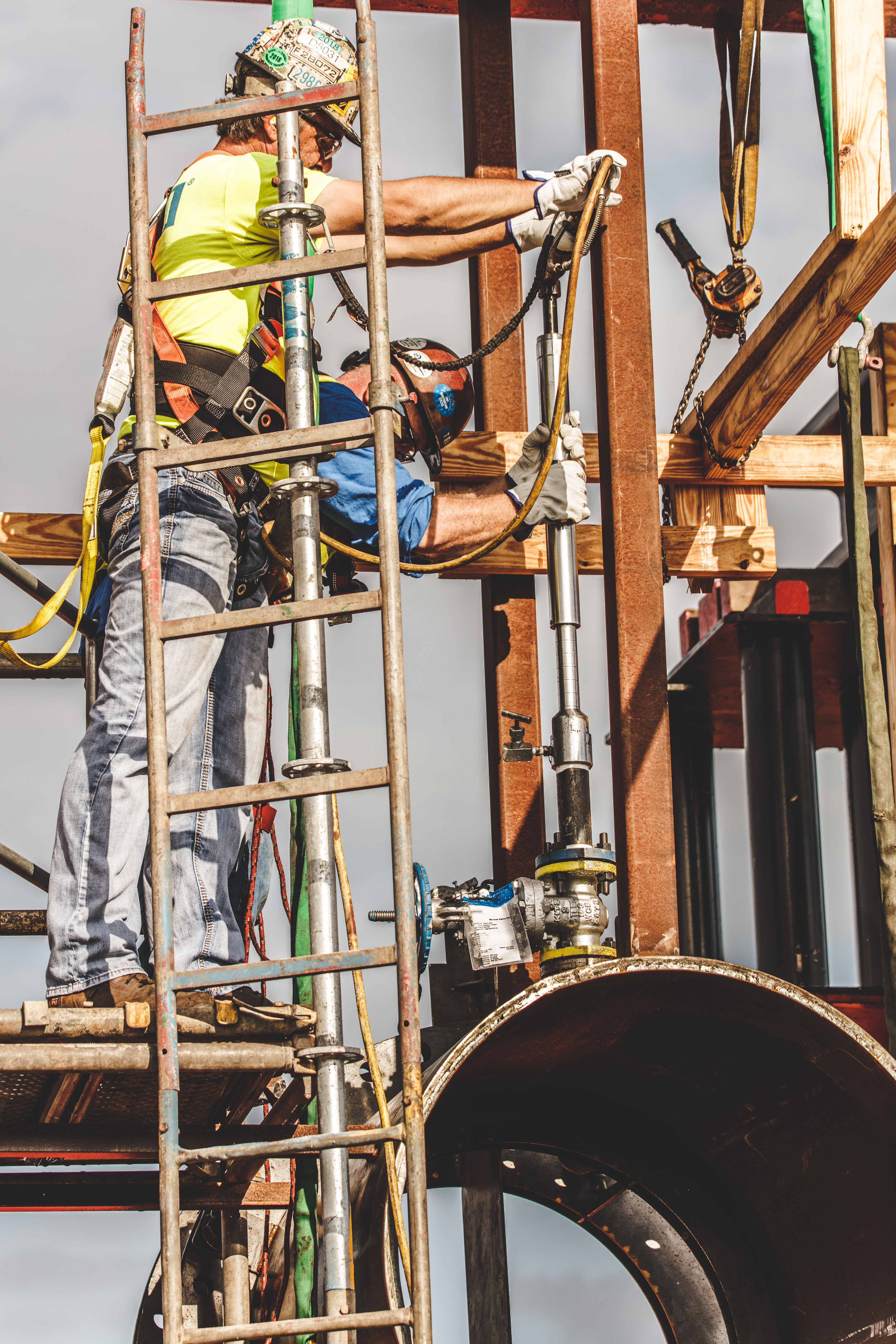 two construction workers with harnesses and hardhats elevated by scaffolding working with steel beams