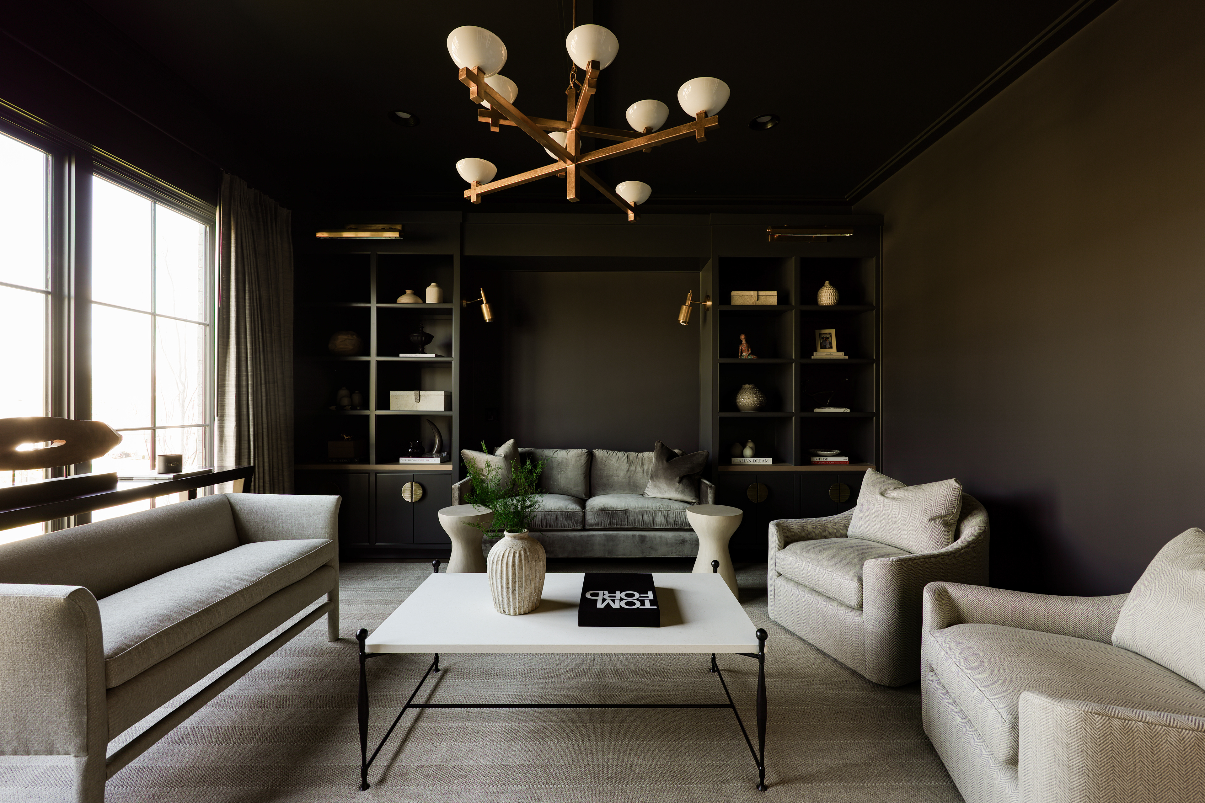 A dark moody living room with gold finishes and neutral seating and natural light