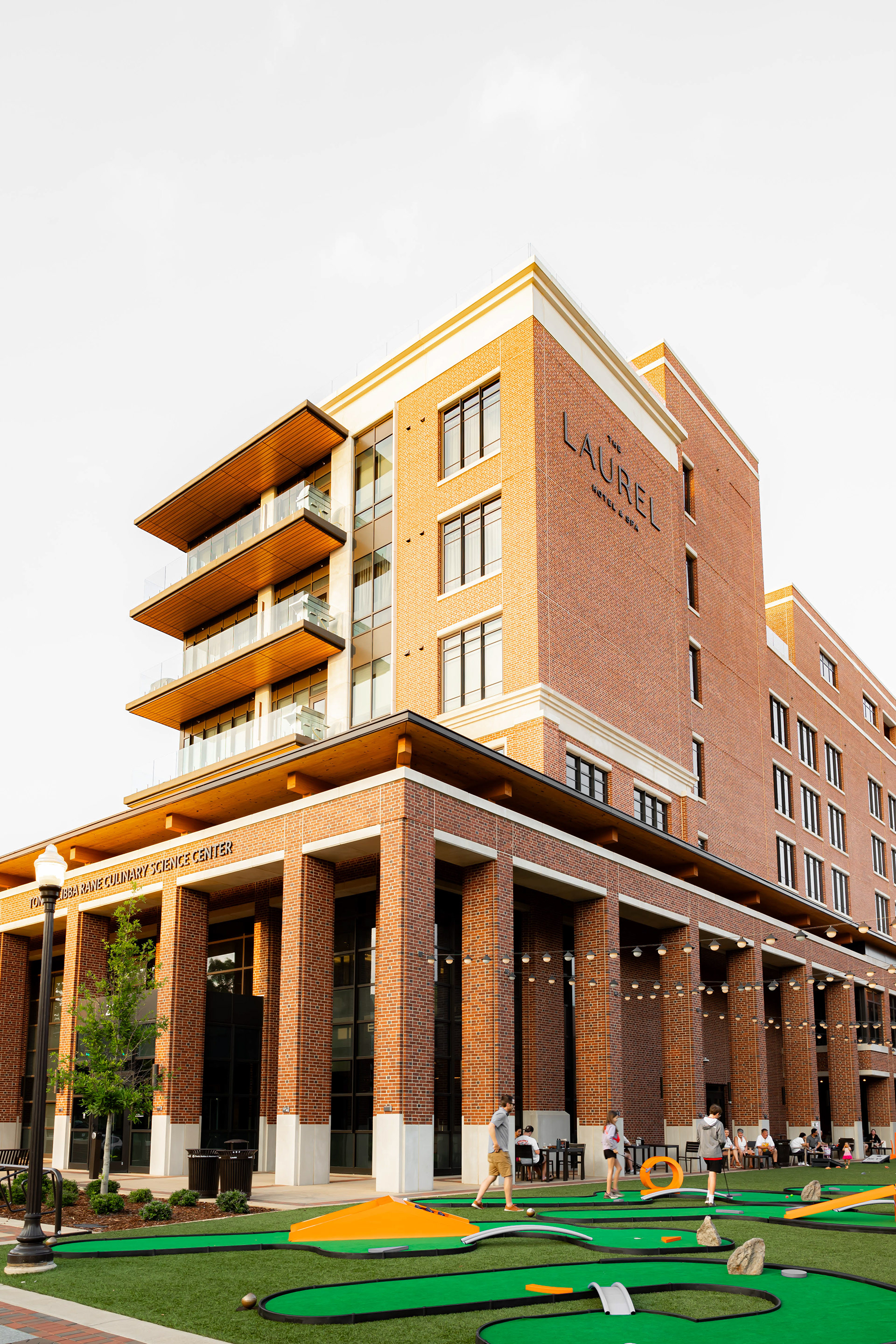 The Laurel Hotel and Spa and The Tonya and Libby Rane Culinary Center from Auburn University Hospitality, with people playing put-put at the Hey Day Market, in downtown Auburn Alabama