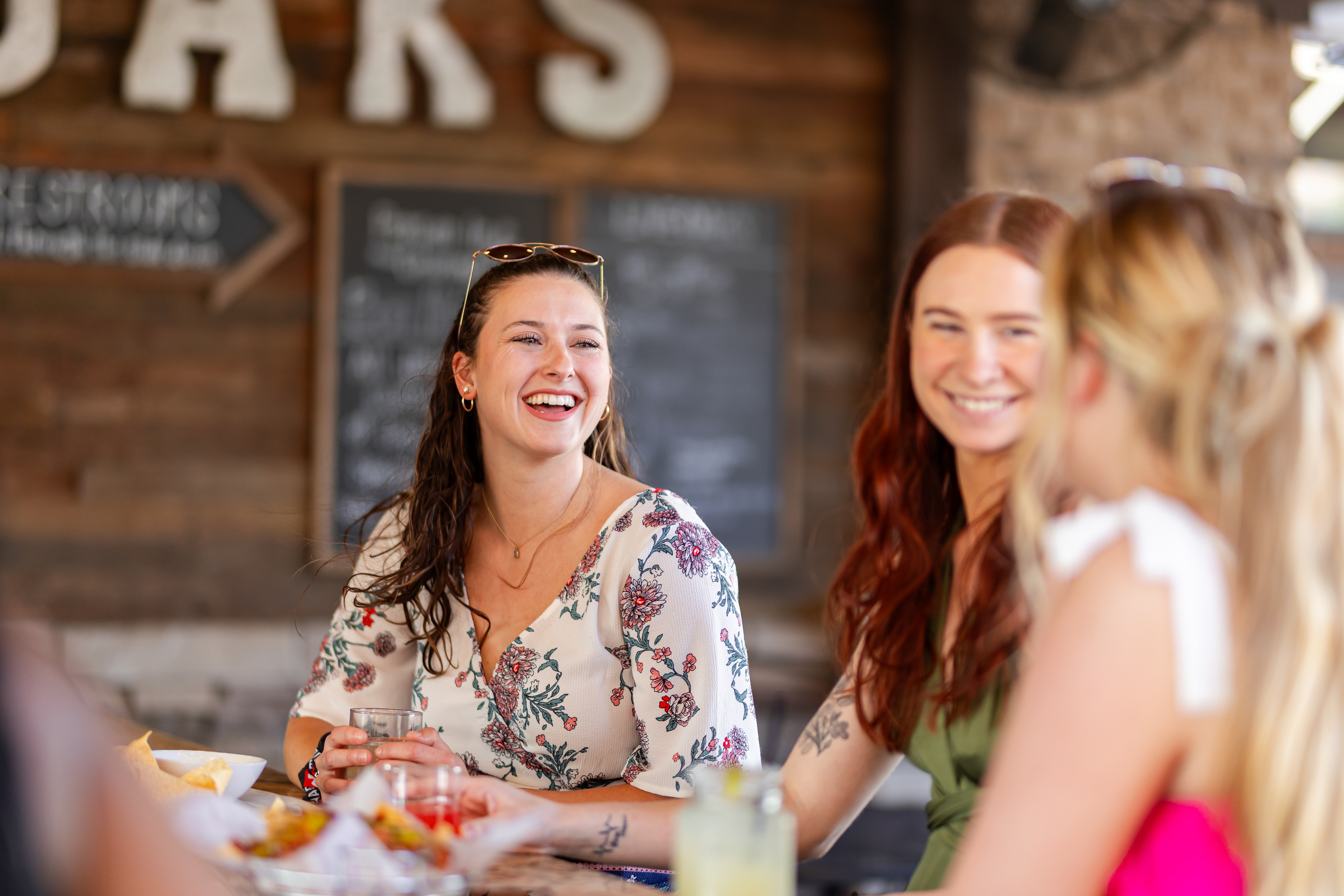 a group of women that are laughing and having drinks and appetizers at Live Oaks in Downtown Auburn, showing patio dining