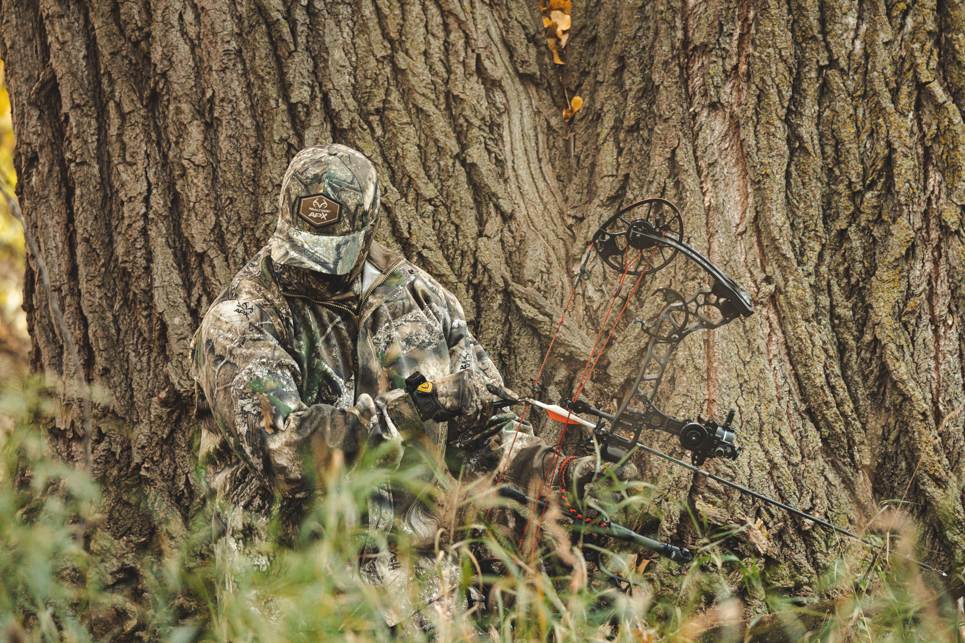 Bow hunter, Melissa Bachman, camoflaged in Realtree APX hunting gear against a large tree