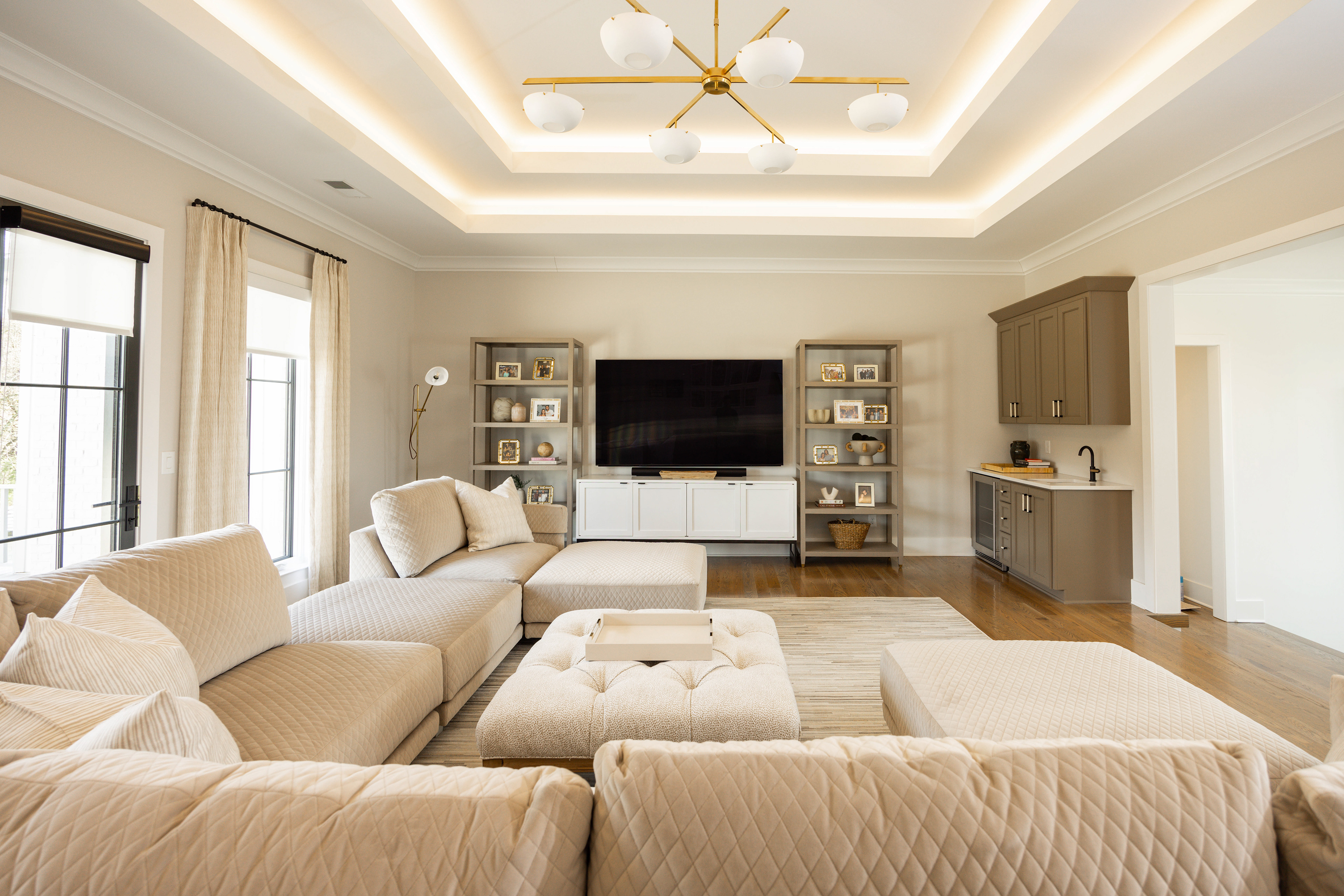 bright warm white living room interior, wide view with quilted sectional, recessed led light strips, taupe colored cabinetry