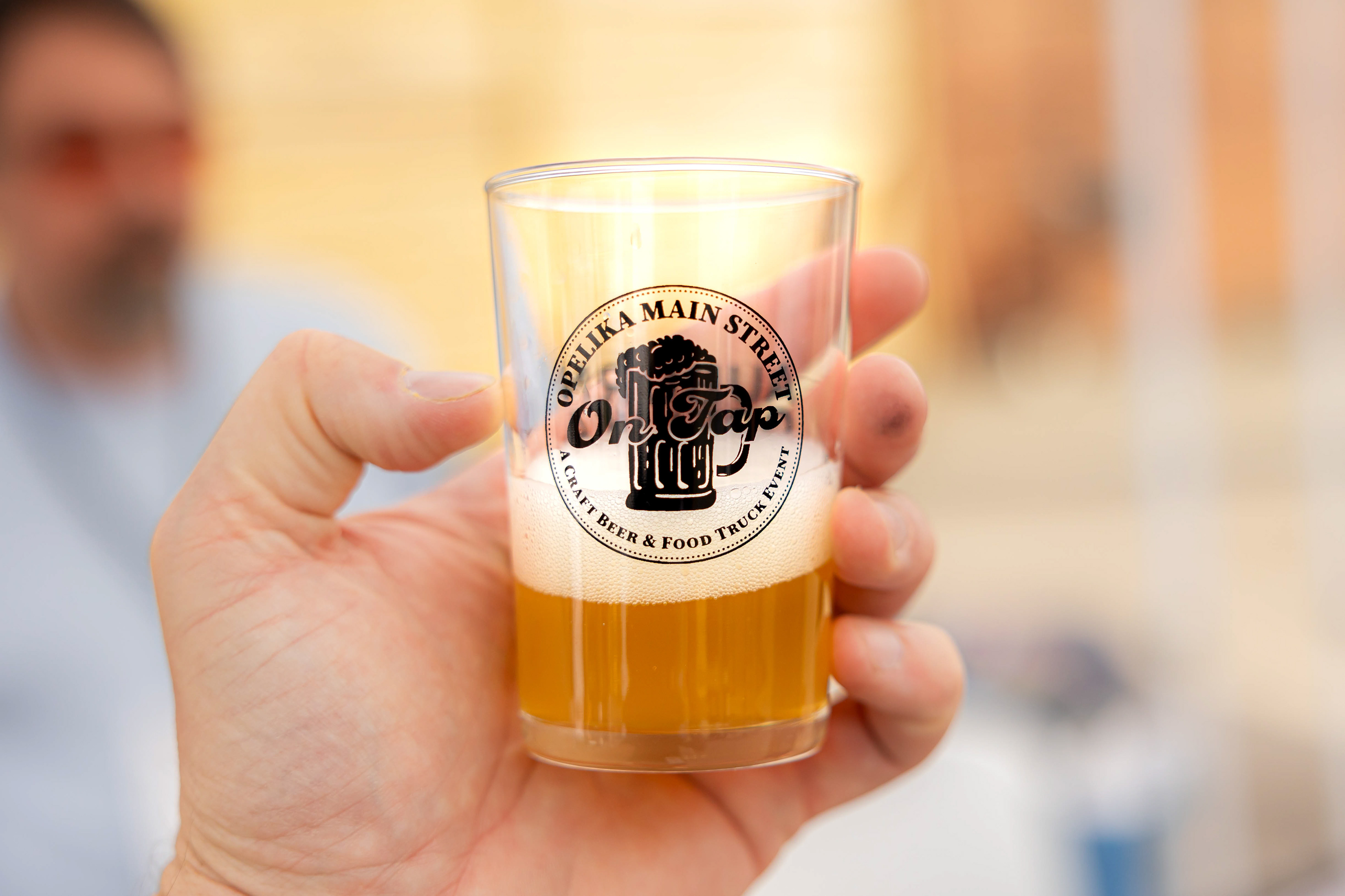 a tight shot of a shot glass that reads "Opelika Main Street On Tap", event merch