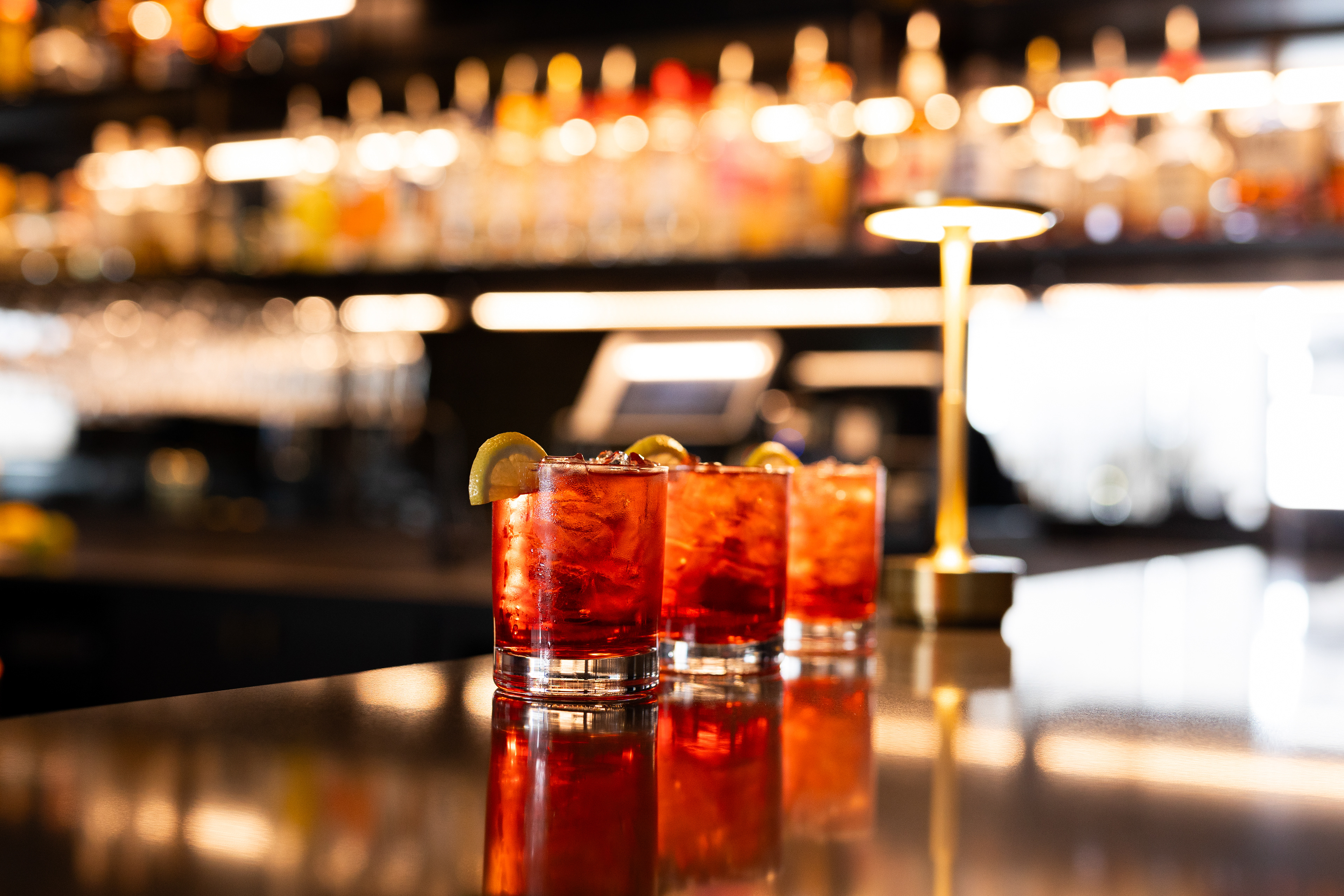 bar interior detail shot of cocktails lined up on the bar, moody with bold colored drinks