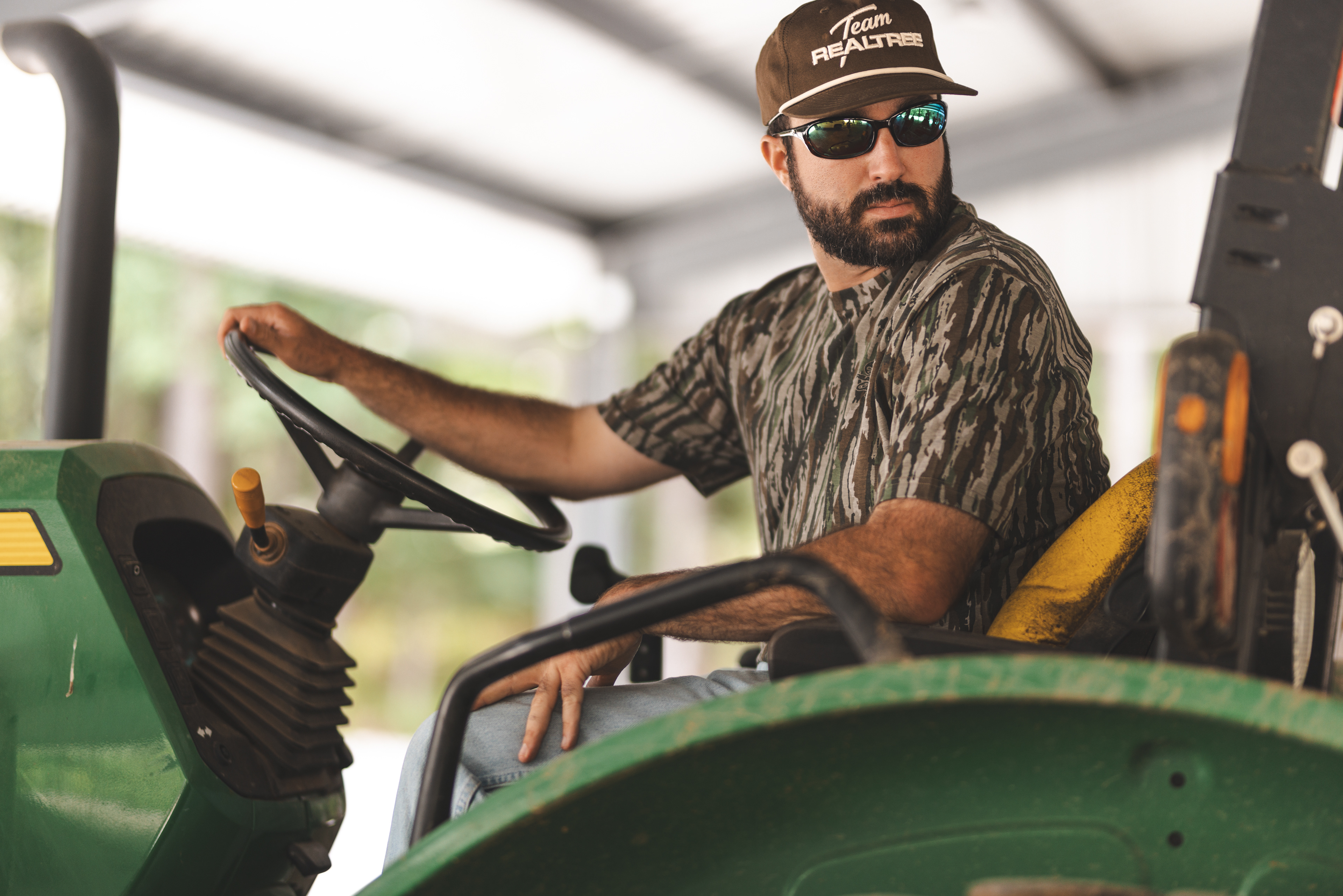 Farmer on a tractor wearing a Realtree camouflage shirt and a hat that reads "Team Realtree"