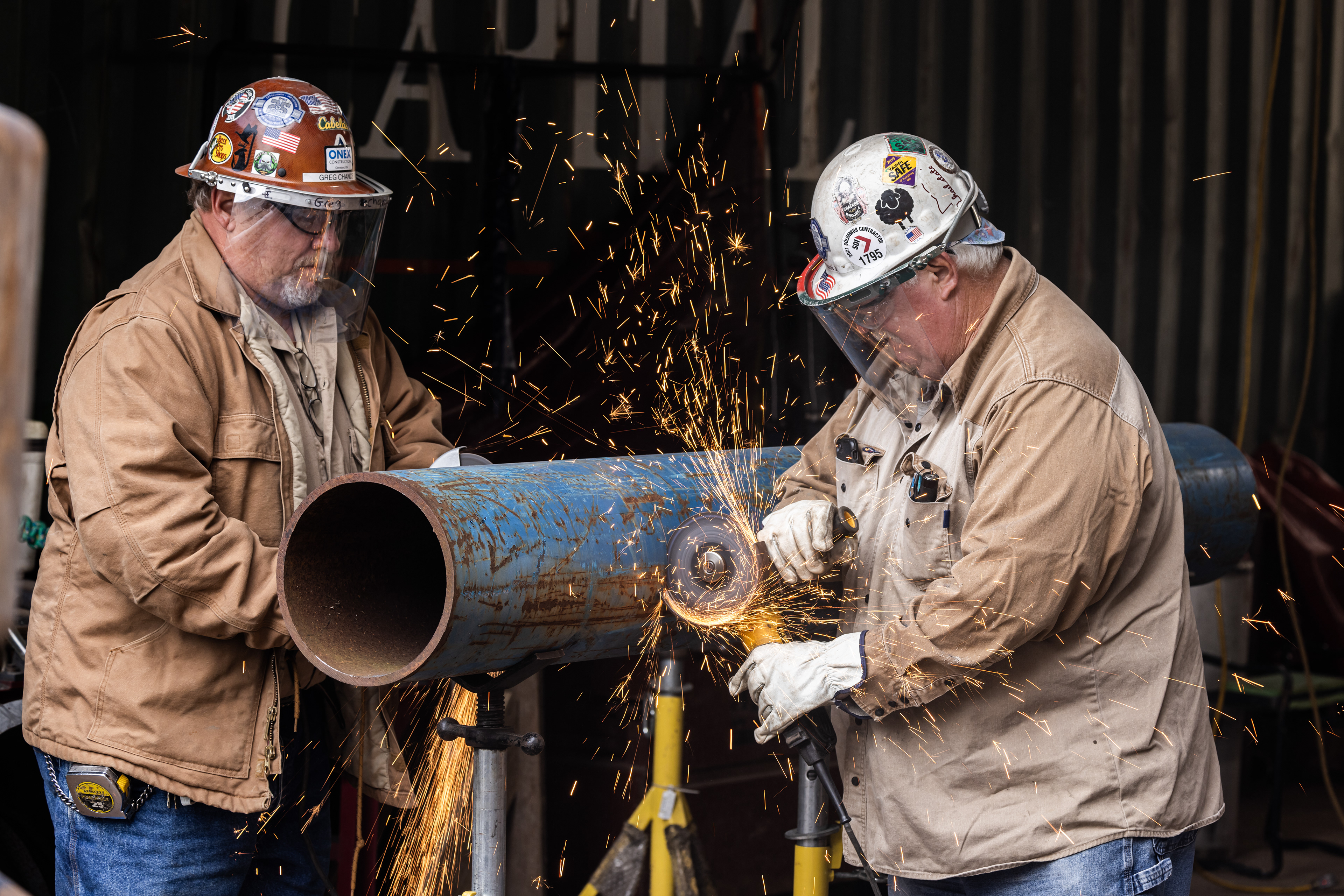 two Barnhart construction workers cutting through a metal pipe with sparks flying