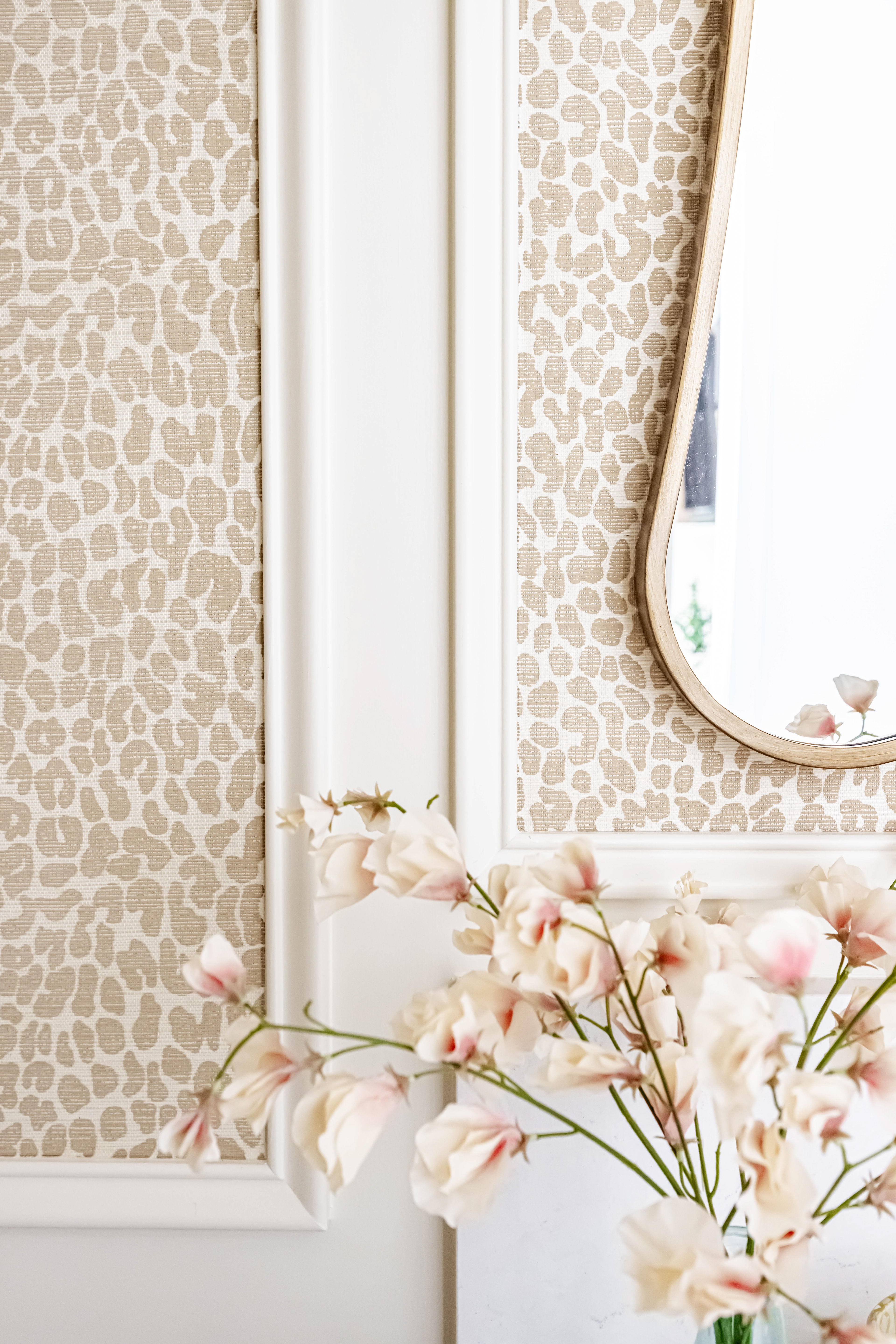 detail shot with white trim, neutral colored leopard print linen textured wall paper, a curved mirror, and faux flowers