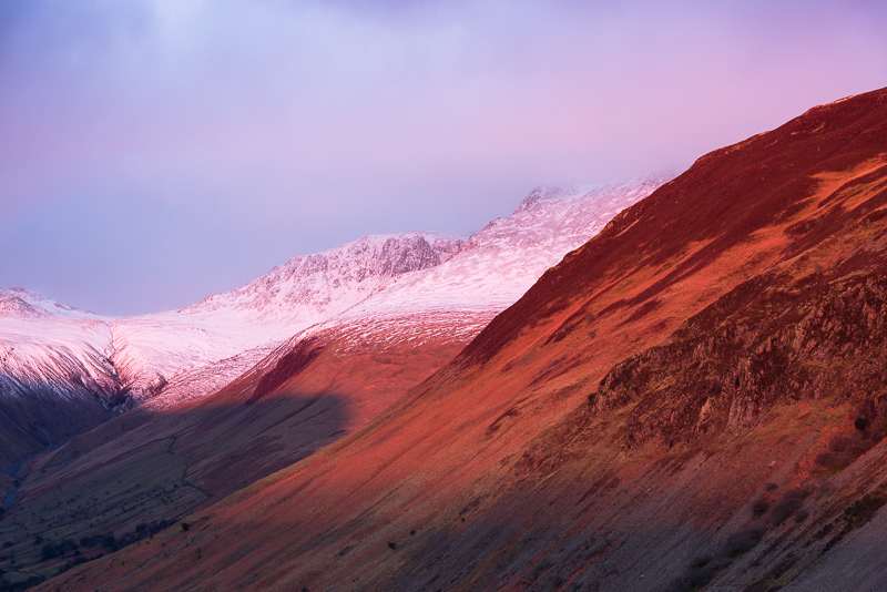 The setting sun casting a red glow on the snow capped mountains above Wastwater in the Lake District. 