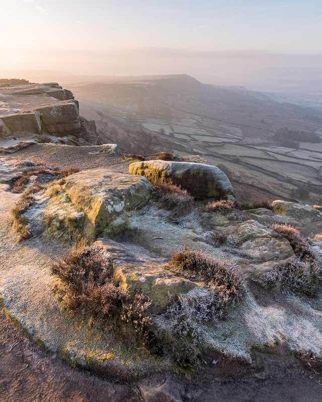 The view from a frozen Curbar Edge, in the Peak District,  with the sun rising with a misty Baslow Edge in the background.