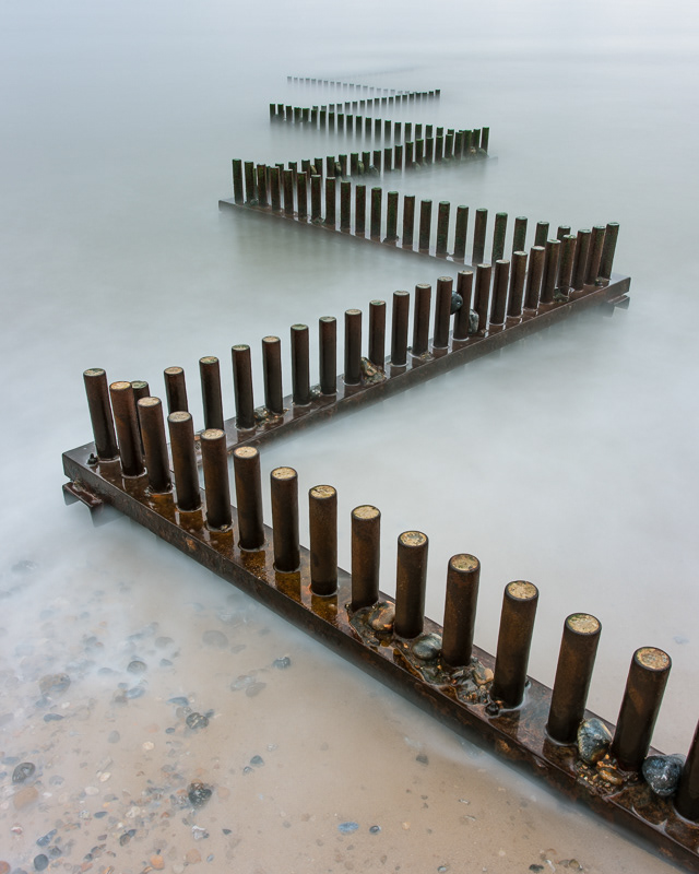 Zig Zag shaped metal groynes on Caiseter beach, Norfolk surrounded by a misty sea.