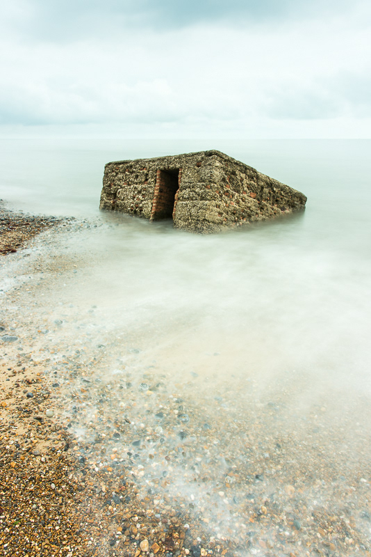 An old pill box disappearing into a smooth sea on Caister beach, Norfolk due to coastal erosion.