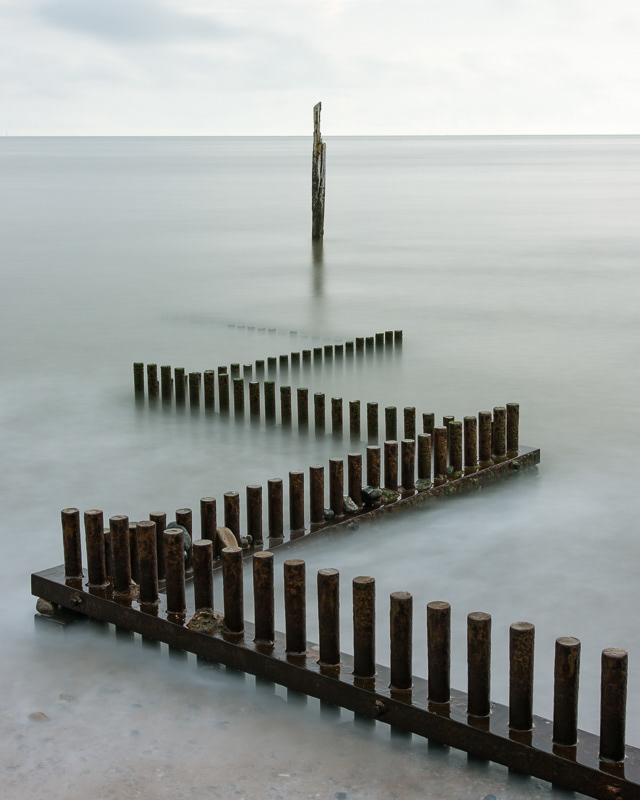 Zig zag groynes and a weathered wooden end post surrounded by smooth sea on Caister beach, Norfolk.