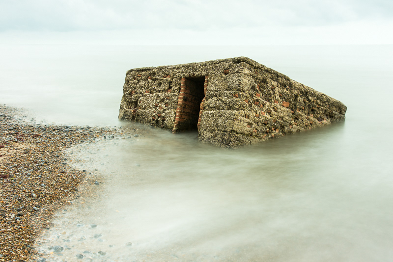 An old pill box slowly disappearing into the smoothed sea on Caister beach, Norfolk.