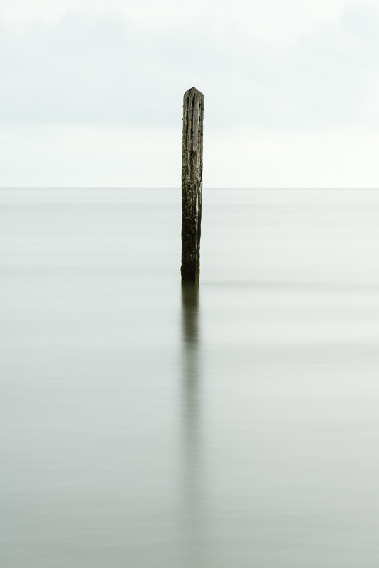 A minimalistic image of a lone weathered wooden post sticking out of a calm sea on Caister beach, Norfolk.