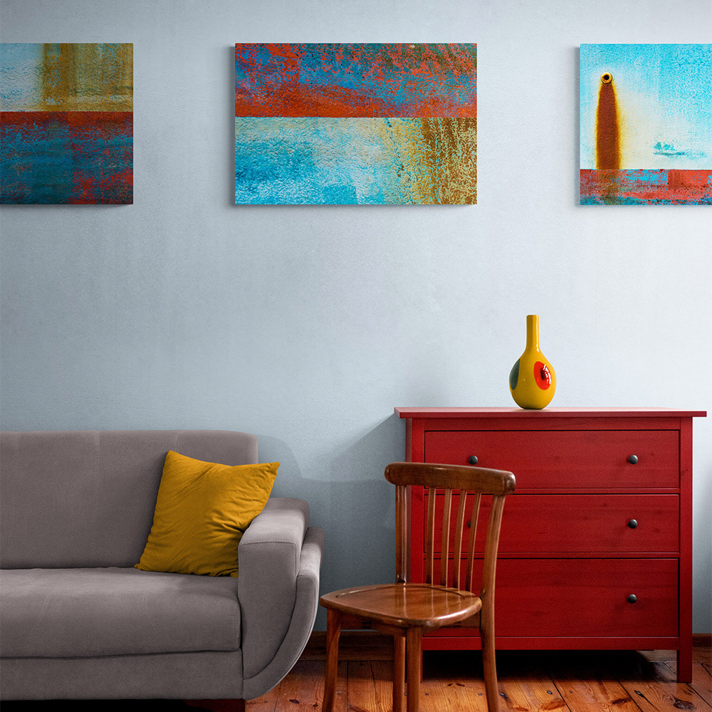 Three textural abstract images of the rusty patina on a fishing boat displayed on a wall over a couch and dresser.
