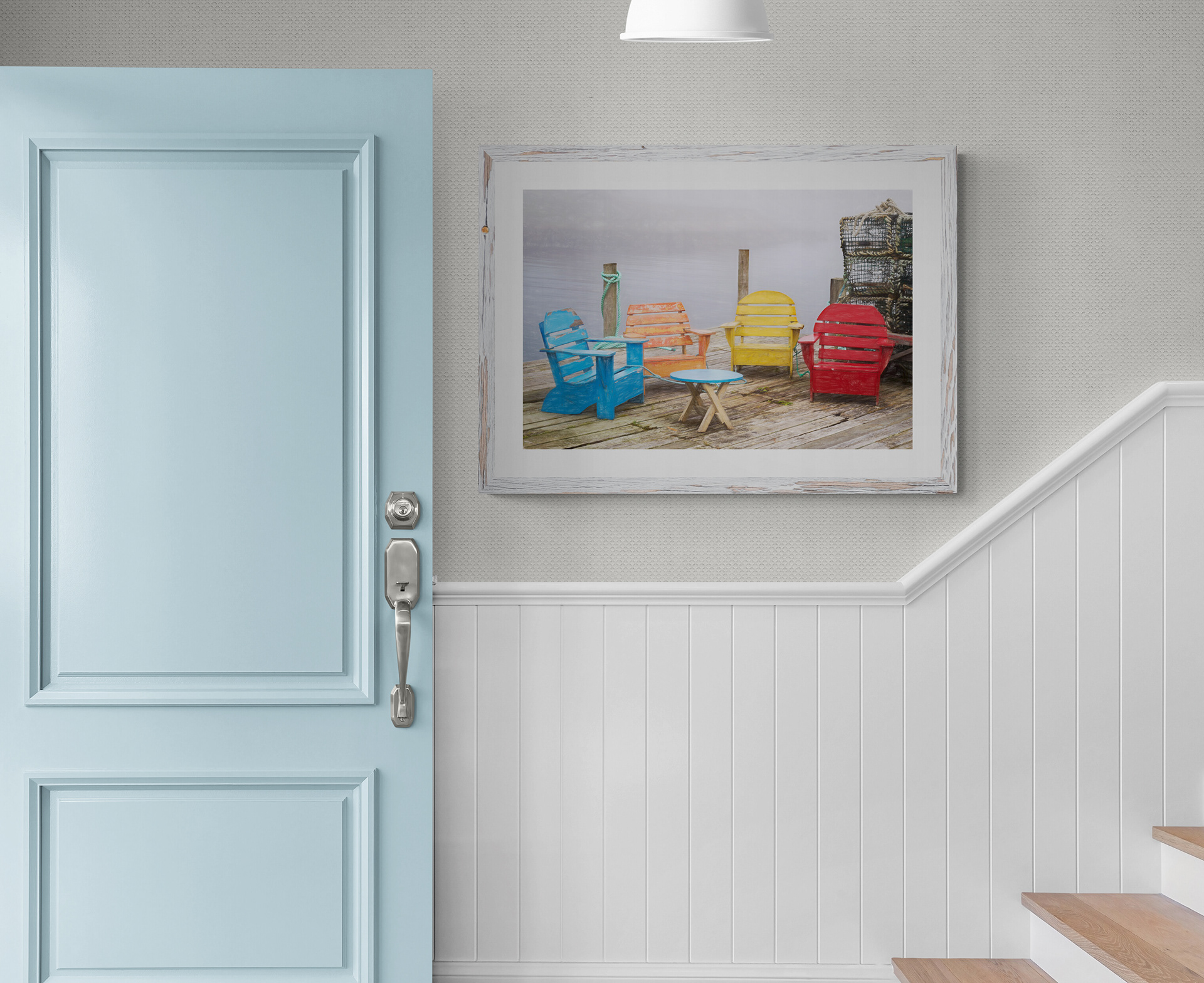 A framed print of 4 colourful wooden chairs on a foggy deck with lobster traps, hanging in a front hall by the stairs.