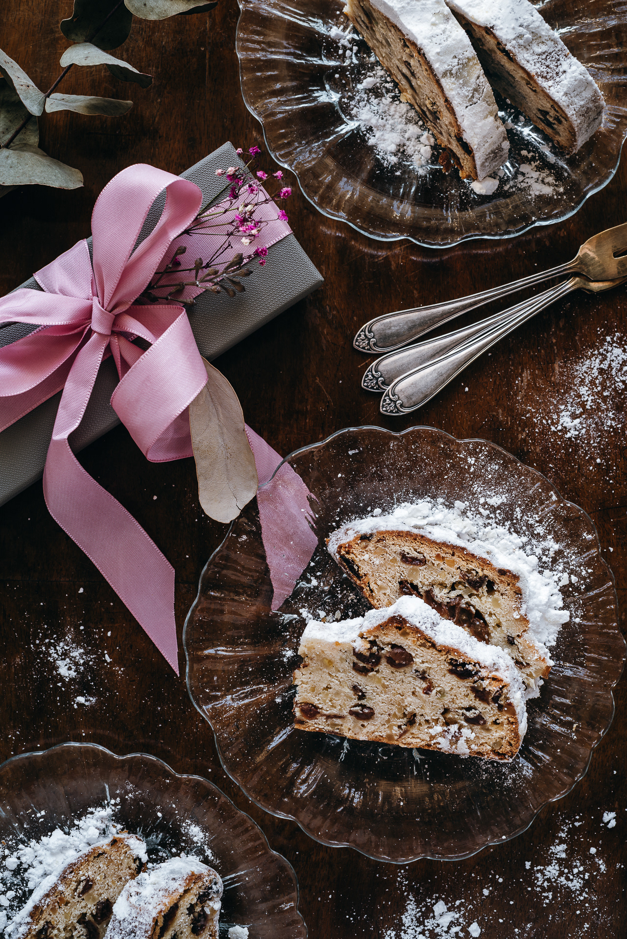 Photo of Christstollen served on crystal plates on an old table, next to a gift with a pink bow – taken by Marta Fochtmann, a food photographer from Frankfurt (Oder) in Germany