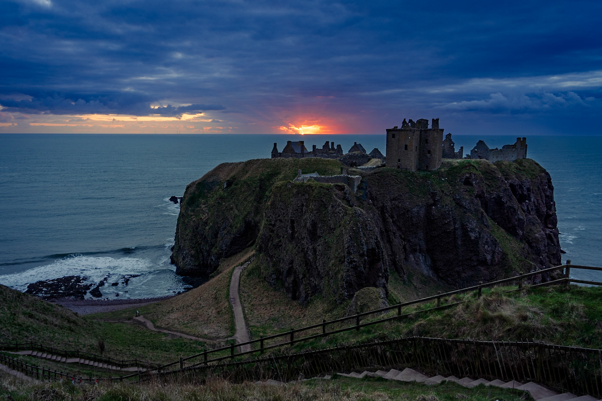 Image of Dunnottar Castle perched on top of a cliff with sea at the back during a dramatic sunrise