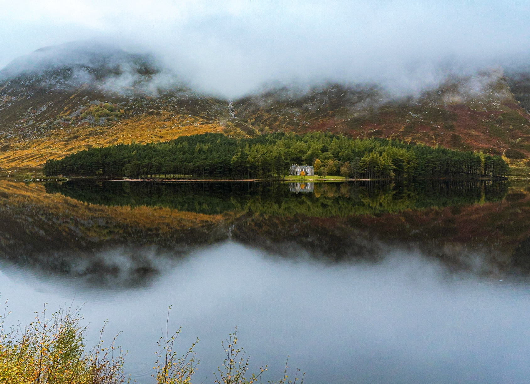 Image of the victorian house by the edge of Loch Muick with the water reflecting the house and the misty mountains during autumn.