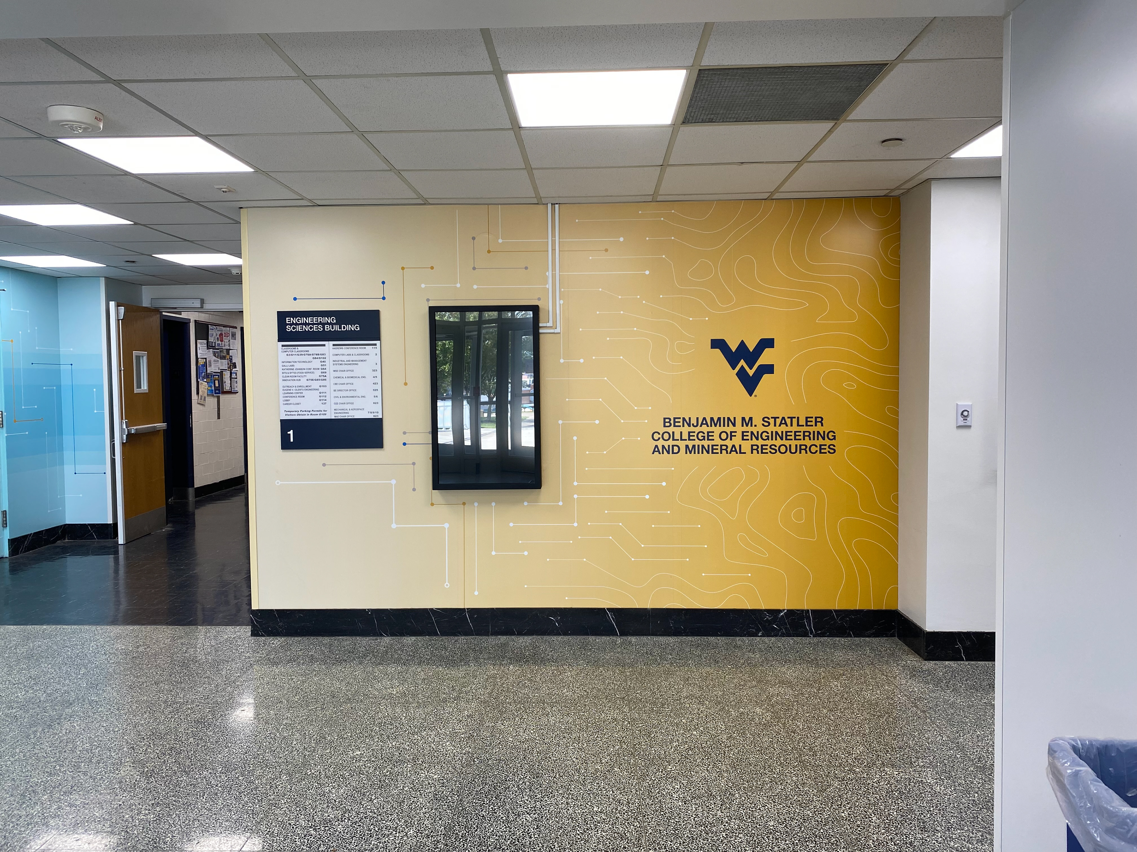The last section of the installed wall, with the digital signage monitor reinstalled back over the vinyl. The circuits in the design wrap around it and the college logo ends the segment.