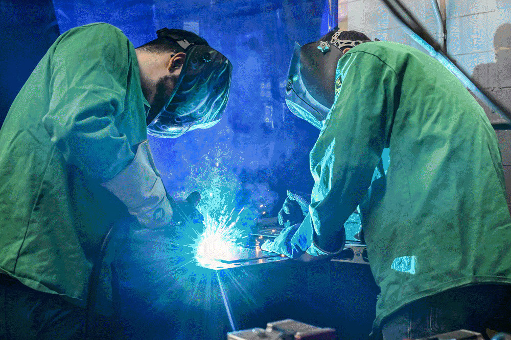 Images spliced together of two students in welding masks and gear intently working on a project as sparks and smoke fly around their work space.