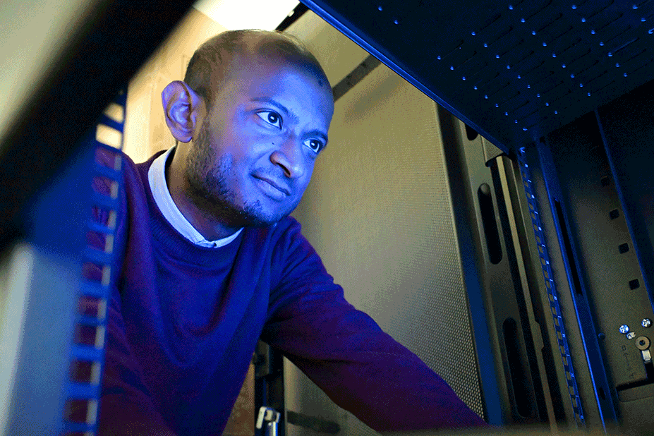 Images spliced together to create a GIF of a student smiling as blue light covers his face while he works on a computer screen.