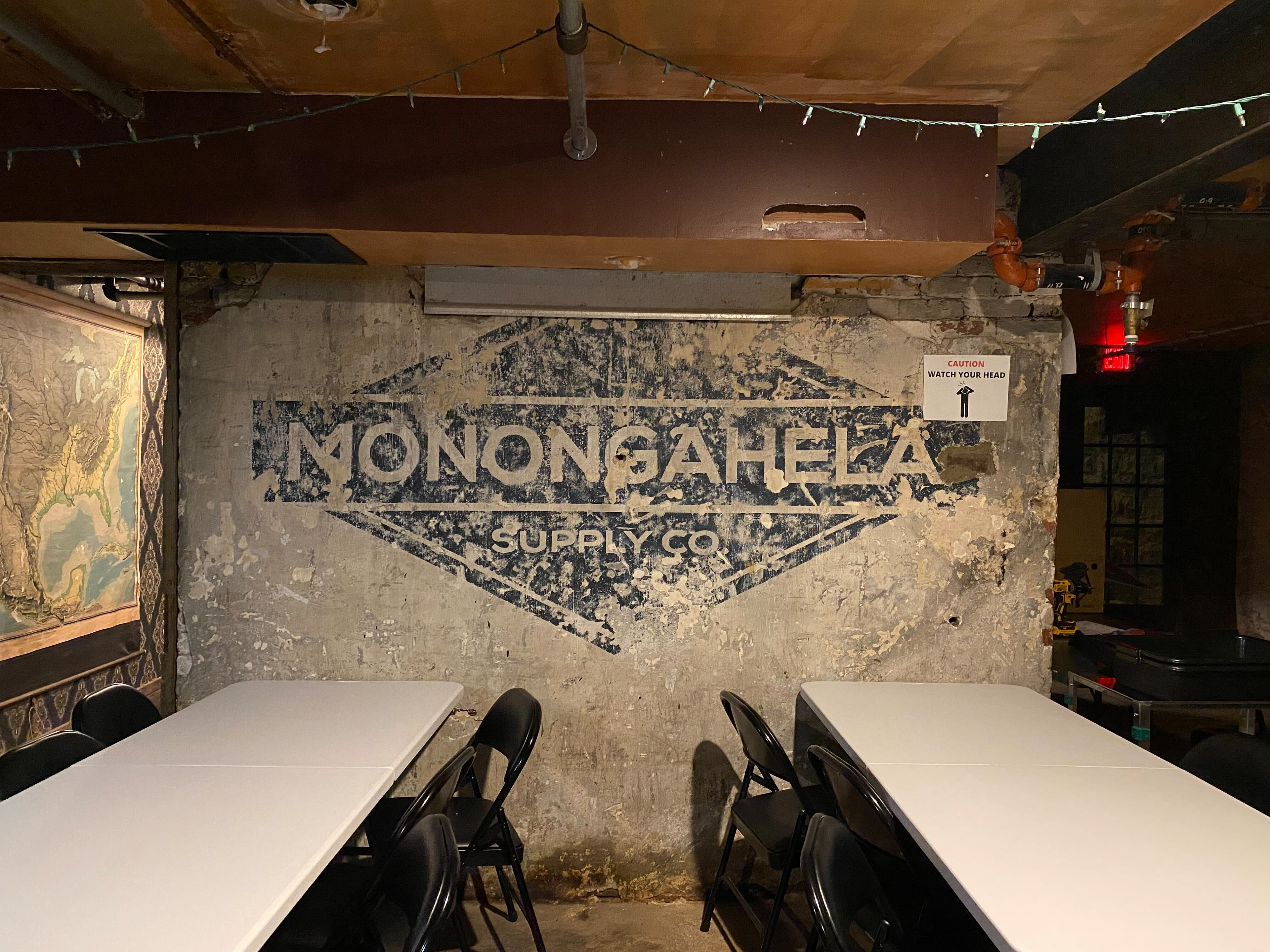 A crumbling concrete wall with tables in front of it, with a fading logo that reads "Monongahela Supply Co.".