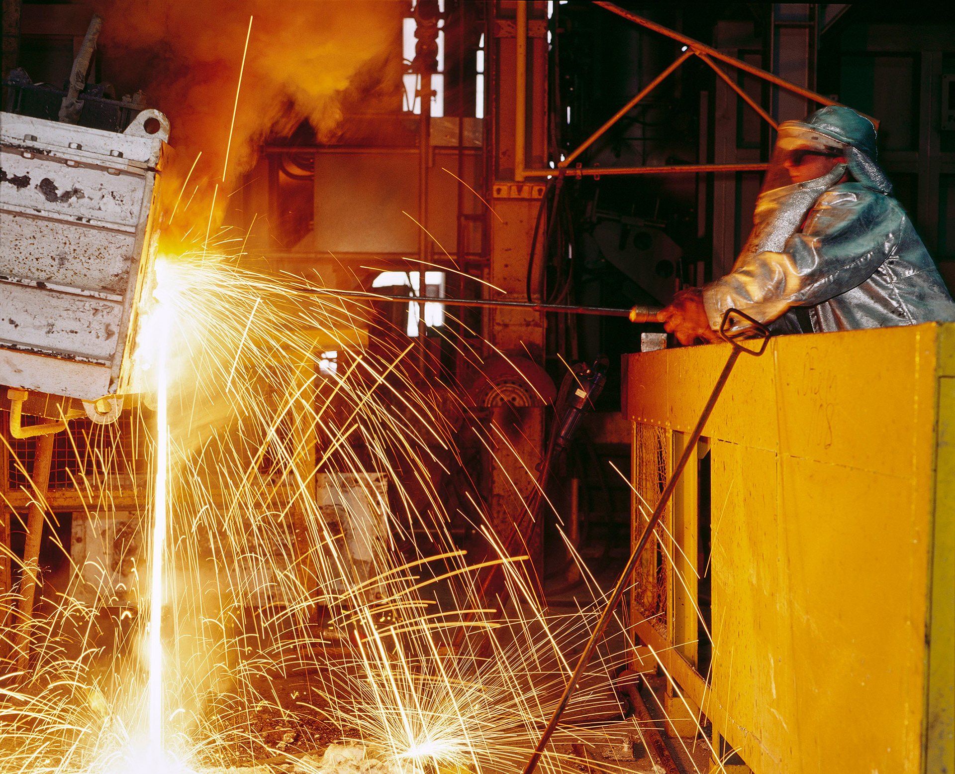 Mann mit Schutzanzug gießt heißes Aluminium in eine Form.  Man in protective suit pours hot aluminum into a mold.  