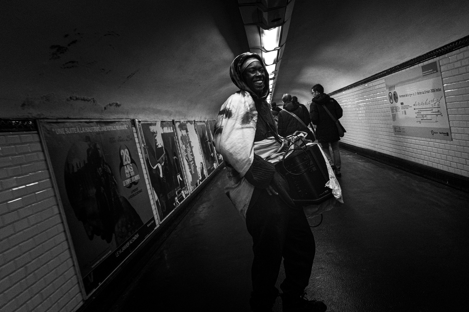 Paris Metro. 11 February 2026. Rose carries in the metro the banner, a speaker and a microphone as she heads towards the Belleville belvedere for the open mic night. This open mic event has been organised in tribute to El Hacen Diarra, who died in police custody following a violent arrest by the police on the night of 15–16 January 2026.