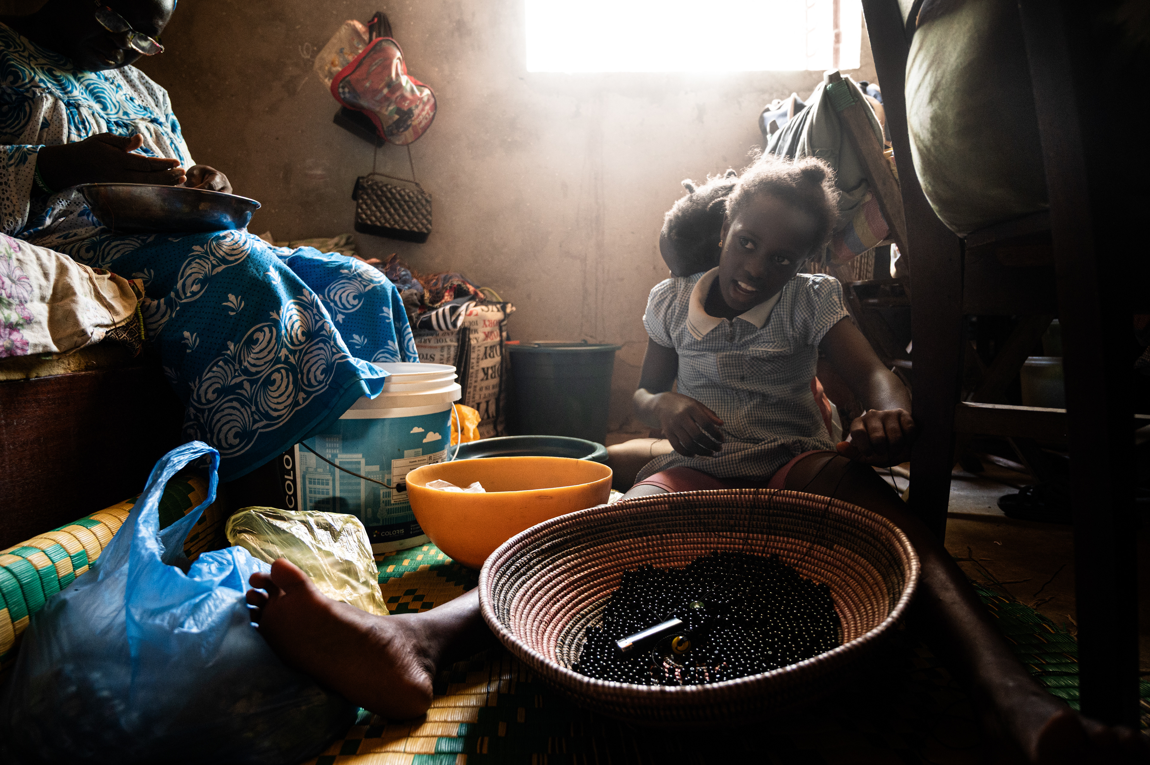 Noura resting her head on Jari’s back whilst they help the adults to make pearl necklaces for the Boukout ceremony in Sengalene village, Casamance reagion, southern Senegal. August 12, 2026.
