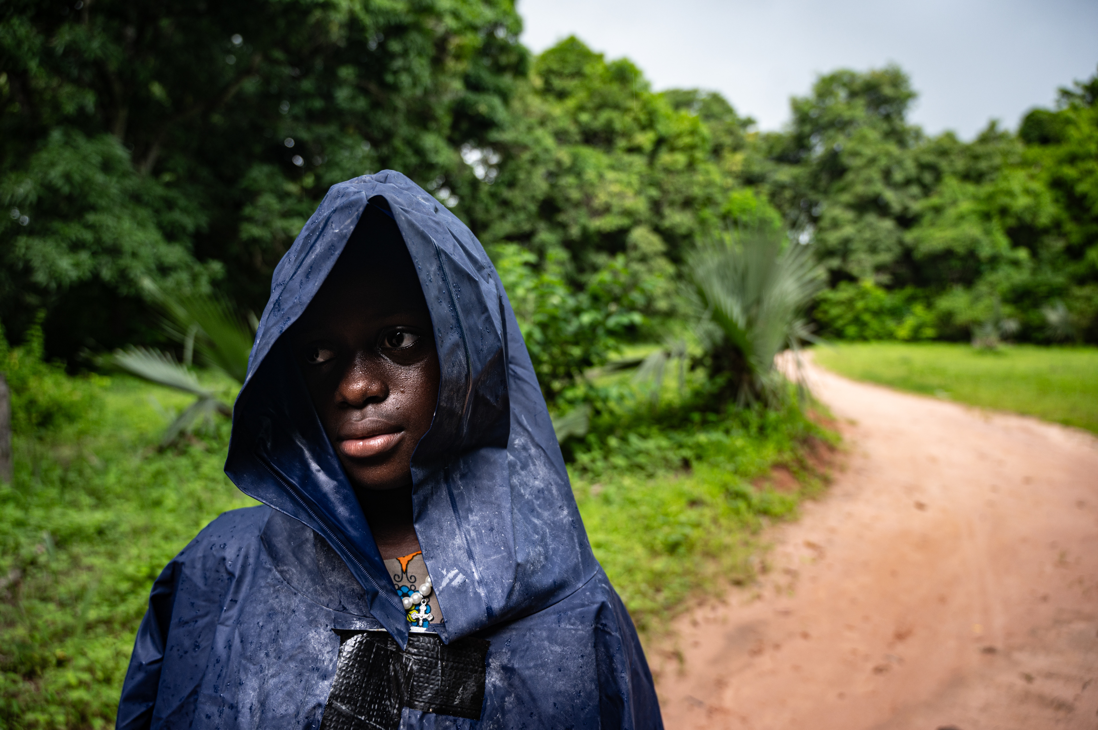 Jari stands under the rain in the middle of a side road during the rainy season in Sengalene village, Casamance region, southern Senegal. August 15, 2026.