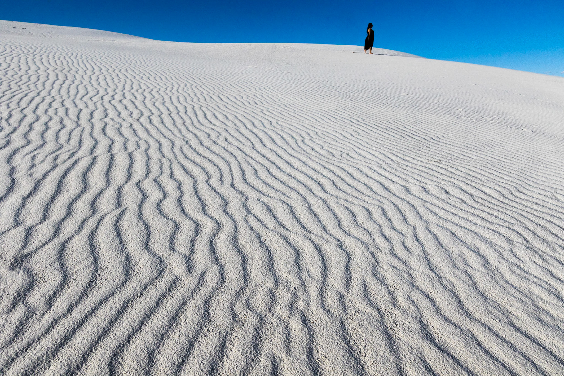 Lone woman in black atop gypsum sand dune, White Sands National Park, New Mexico, USA (3/2020)