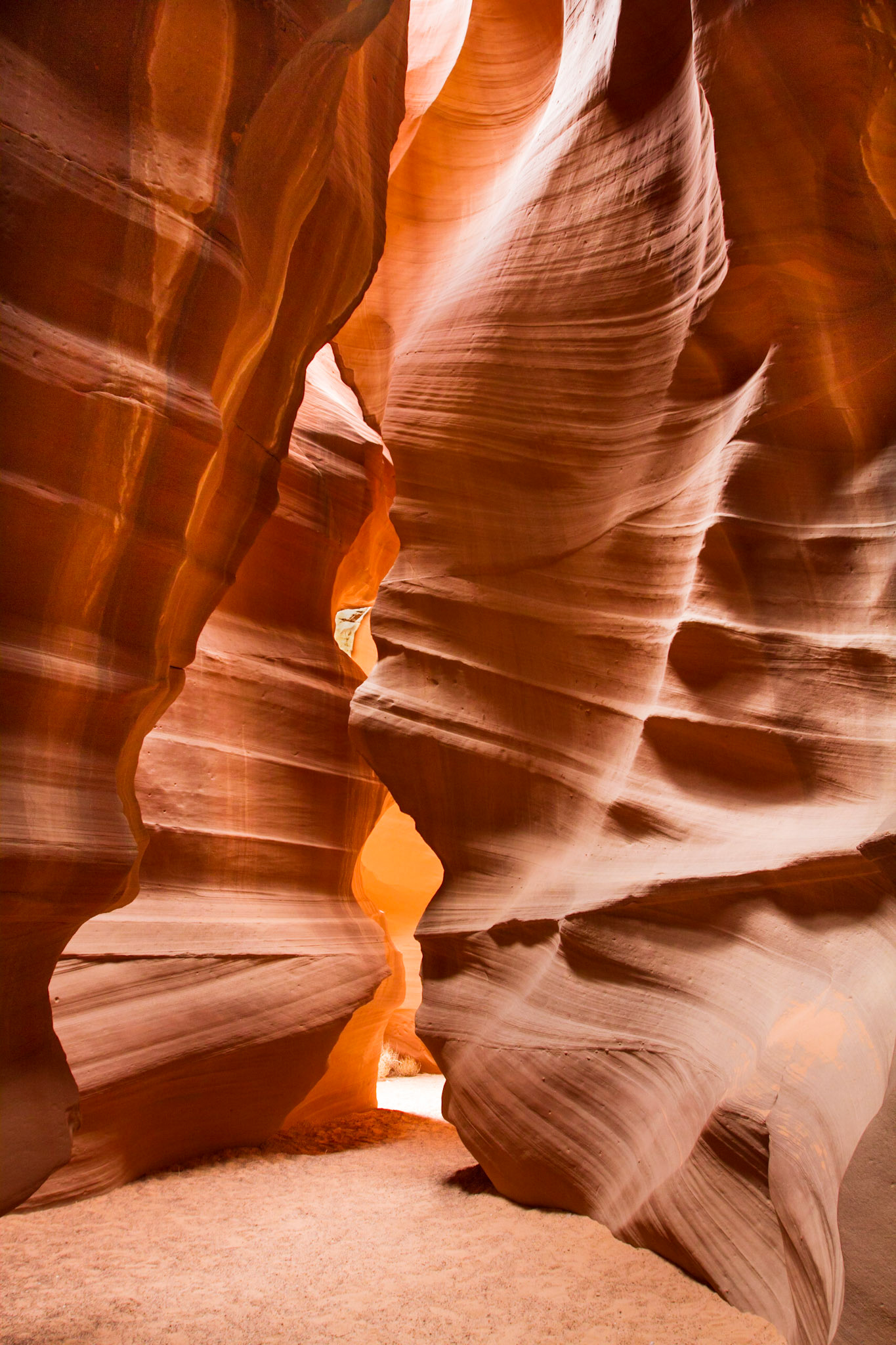 Upper Antelope Canyon is located on Navajo land near Page, Arizona within the LeChee Chapter of the Navajo Nation.  Antelope Canyon includes two separate, slot canyon sections – one on either side of Route AZ98 a few miles East of Page.  These canyons are referred to individually as Upper Antelope Canyon or The Crack; and Lower Antelope Canyon or The Corkscrew.The Navajo name for Upper Antelope Canyon is Tsé bighánílíní, which means "the place where water runs through rocks" and water is what created the canyons as it flowed through and eroded the Navajo Sandstone.  This primarily happens during flash flooding.  Rainwater, especially during monsoon season, runs into the extensive basin above the slot canyon sections, picking up speed and sand as it rushes into the narrow passageways. Over time the passageways are eroded away, making the corridors deeper and smoothing hard edges in such a way as to form characteristic 'flowing' shapes in the rock.Flooding in the canyon still occurs. A flood occurred on October 30, 2006 that lasted 36 hours, and caused the Tribal Park Authorities to close Lower Antelope Canyon for five months.
