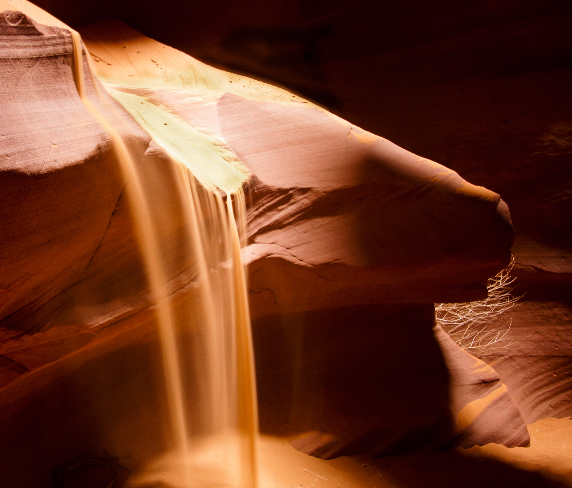 Sand Falling in Upper Antelope Slot Canyon, Page, AZ.  During tours of the canyon guides toss sand onto the top of this rock and let it flow over the edge in as Sandfall. Upper Antelope Canyon is located on Navajo land near Page, Arizona within the LeChee Chapter of the Navajo Nation.  Antelope Canyon includes two separate, slot canyon sections – one on either side of Route AZ98 a few miles East of Page.  These canyons are referred to individually as Upper Antelope Canyon or The Crack; and Lower Antelope Canyon or The Corkscrew.The Navajo name for Upper Antelope Canyon is Tsé bighánílíní, which means "the place where water runs through rocks" and water is what created the canyons as it flowed through and eroded the Navajo Sandstone.  This primarily happens during flash flooding.  Rainwater, especially during monsoon season, runs into the extensive basin above the slot canyon sections, picking up speed and sand as it rushes into the narrow passageways. Over time the passageways are eroded away, making the corridors deeper and smoothing hard edges in such a way as to form characteristic 'flowing' shapes in the rock.Flooding in the canyon still occurs. A flood occurred on October 30, 2006 that lasted 36 hours, and caused the Tribal Park Authorities to close Lower Antelope Canyon for five months.