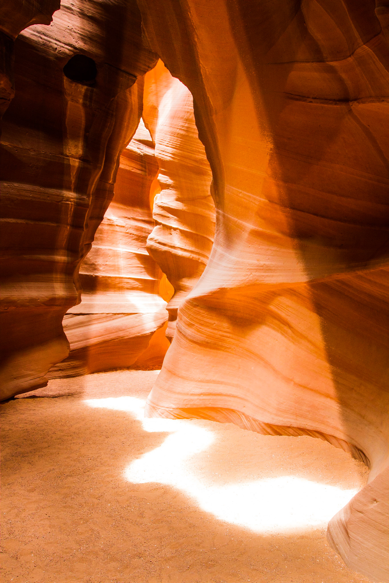 At Antelope Canyon in Page, AZ there are actually dozens of similar slot canyons, the most famous of which is Upper Antelope Canyon.  This canyon can get quite crowded in late morning when the famous "Light Beam" comes along and after throwing dust in the air you can see the narrow shaft of light descending to the canyon floor.This shot was also in Upper Antelope Canyon but is not the standard light beam one usually sees.  The day I was in the canyon the famous light beam didn't materialize due to cloud cover.  However an hour later, after most of the disappointed other photographers had left, in another part of the same canyon, I found this interesting sun pattern on the floor.  While not a column of light like the “Beam” it is more an abstract shape that echoes the shape of the canyon walls (which of course is what makes the shape in the first place).