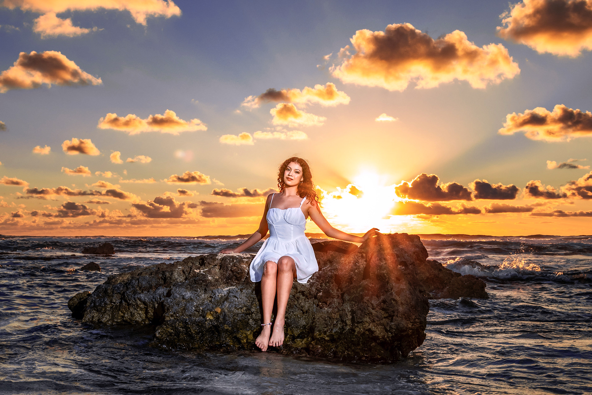 Joven vestida con un vestido blanco en una roca sobre el mar al amanecer