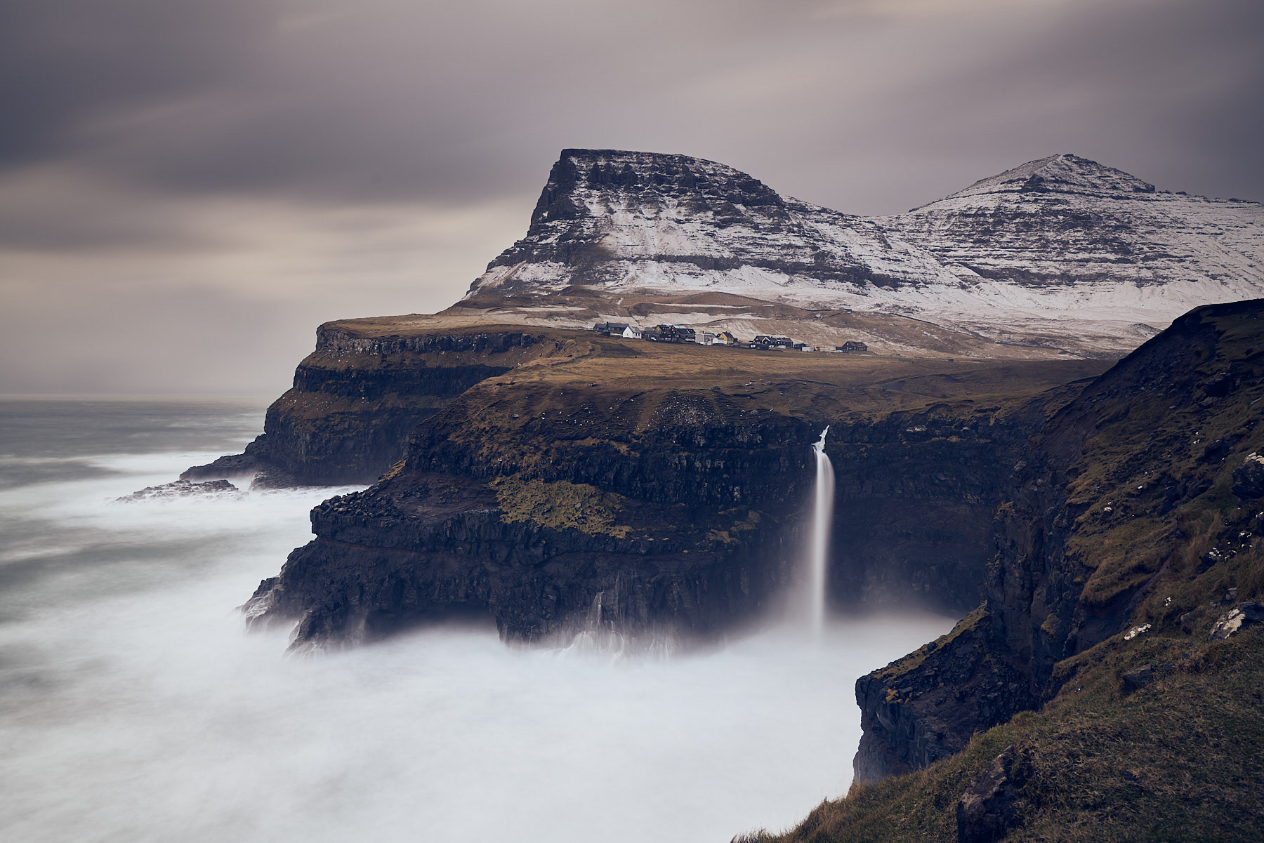 The tiny village of Gásadalur in the Faroe Islands sits at the edge of a tall cliff overlooking the sea.