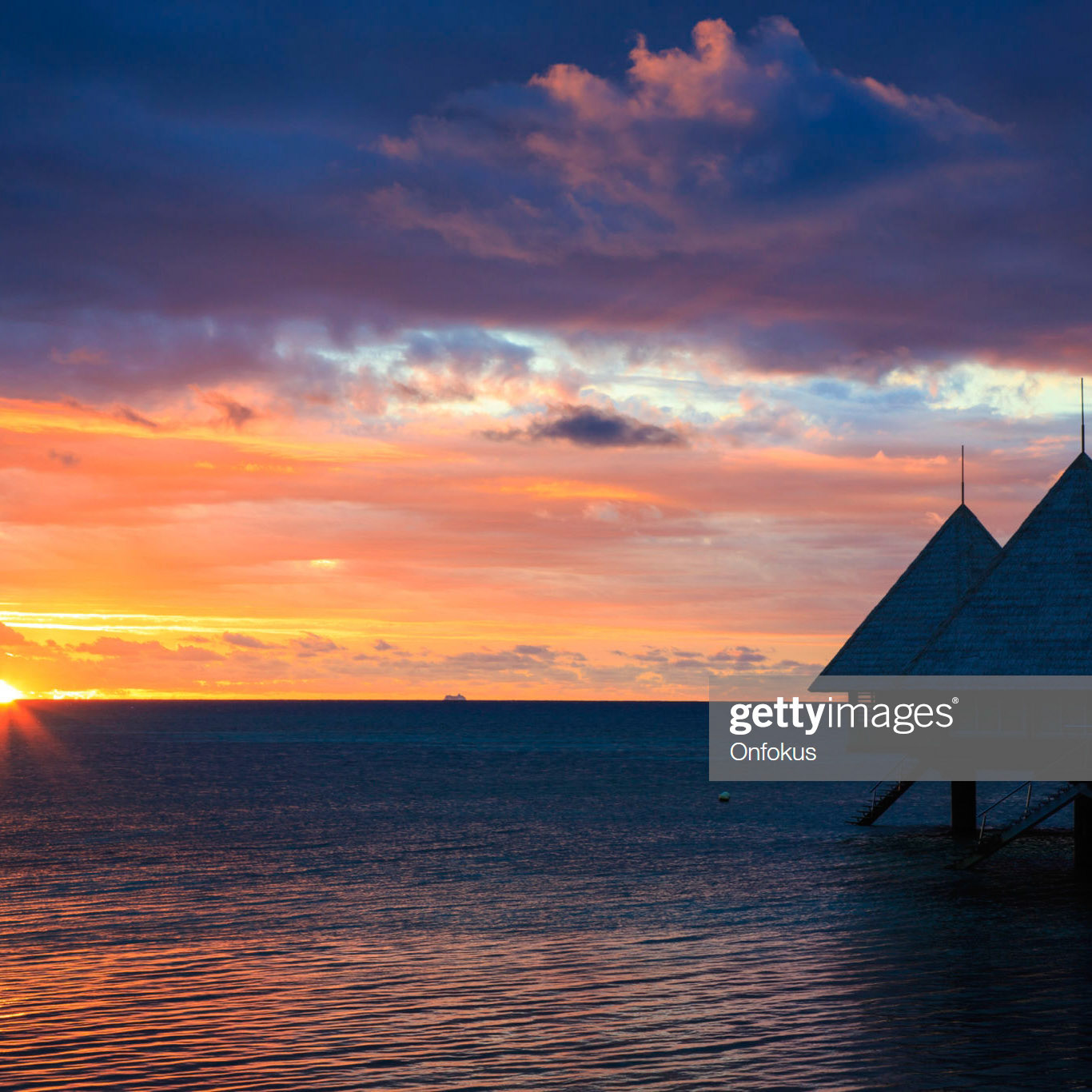 DSLR picture of a Luxury over water bungalow inside a lagoon at sunset.  The bungalow is in the foreground, the water is reflecting the sky. The sky is dark blue and orange.