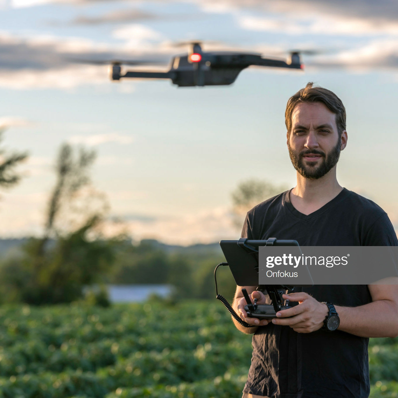 Man Pilot Using a Drone Remote Controller with a digital tablet at Sunset in a field.