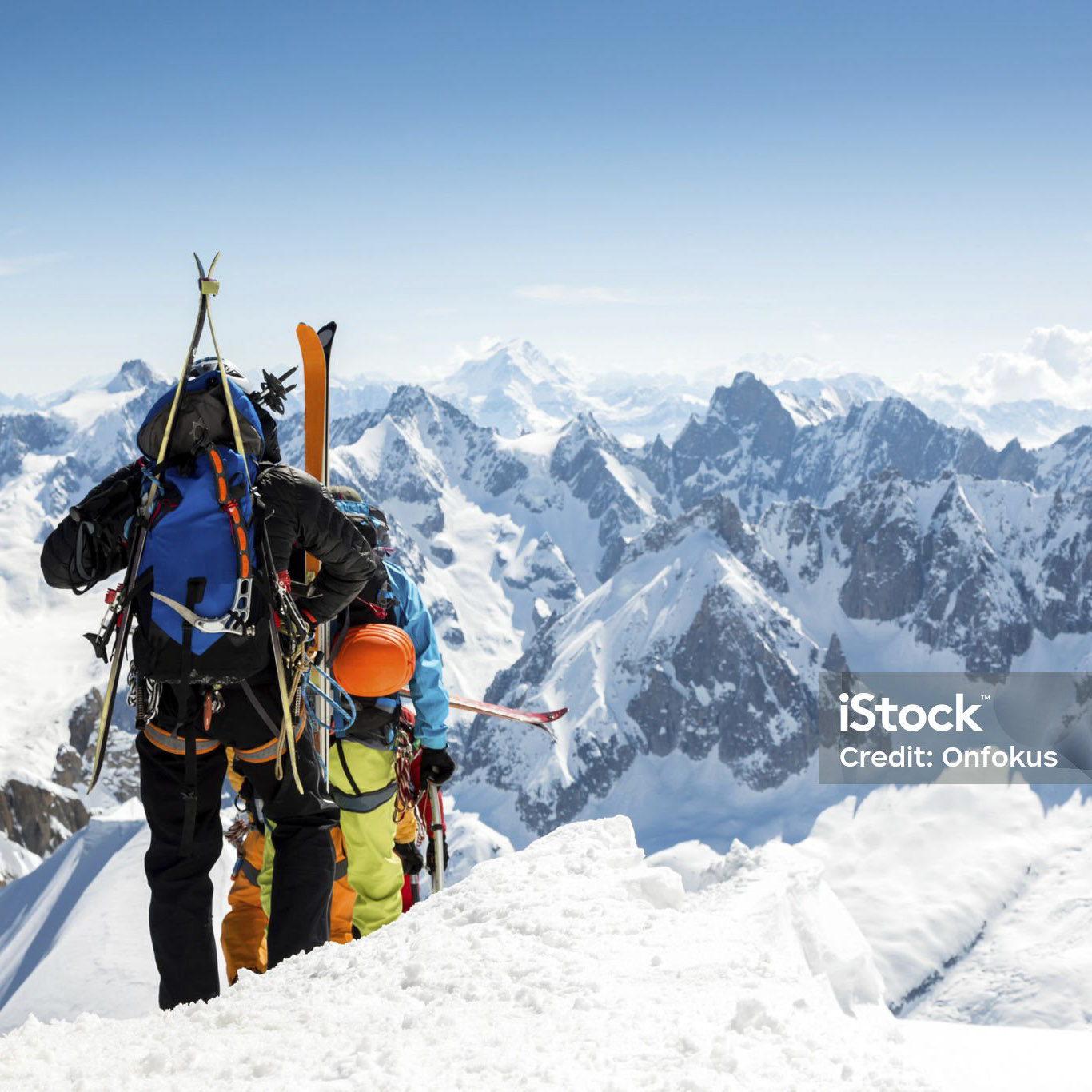 DSLR picture of Alpine climbers going down the ridge at l'Aiguille du Midi to reach the Mont Blanc summit. The climbers are on the foreground and the alps are in the background and the sky is clear.